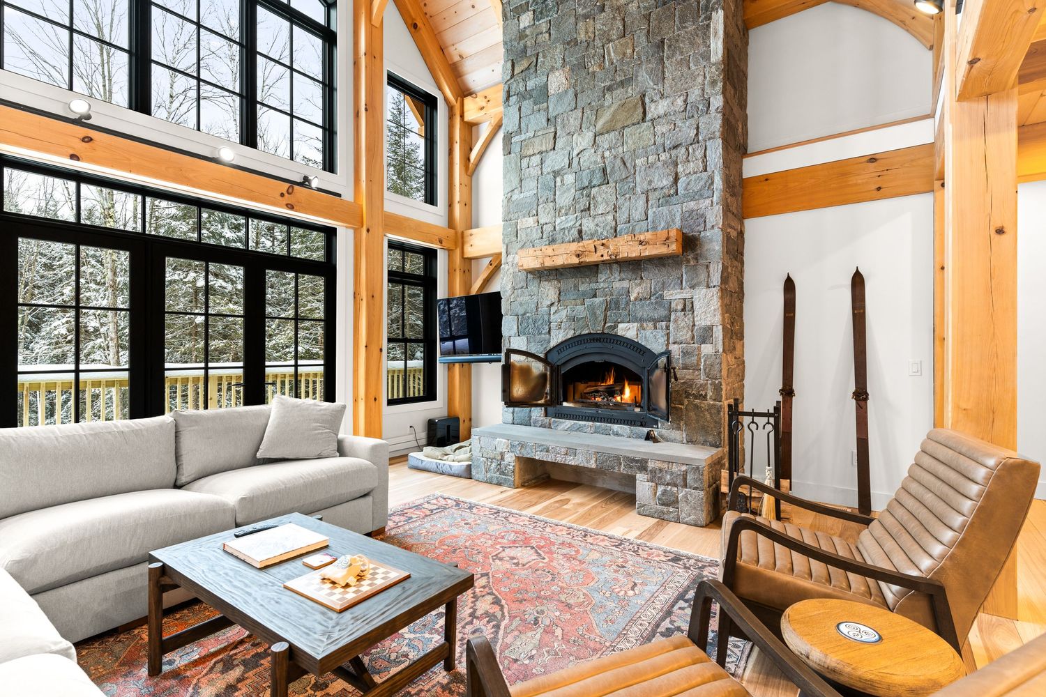 Rustic living room with stone fireplace, large windows, exposed beams, and modern sectional sofa.