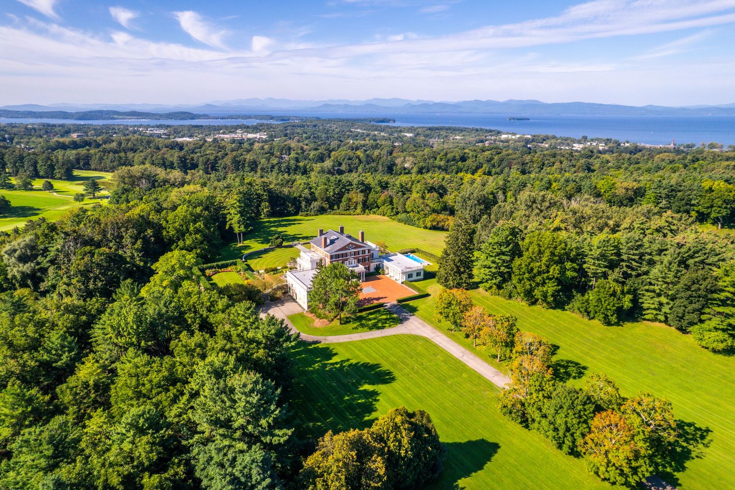 Sweeping aerial view of a luxury estate surrounded by green landscapes and distant mountains.