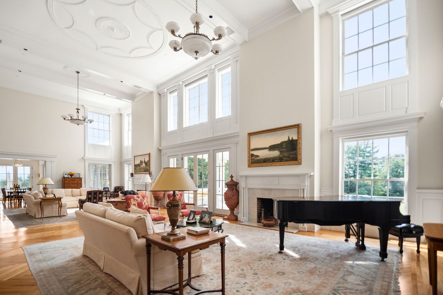 Spacious white living room with high ceilings, grand piano, and abundant natural light streaming through windows.