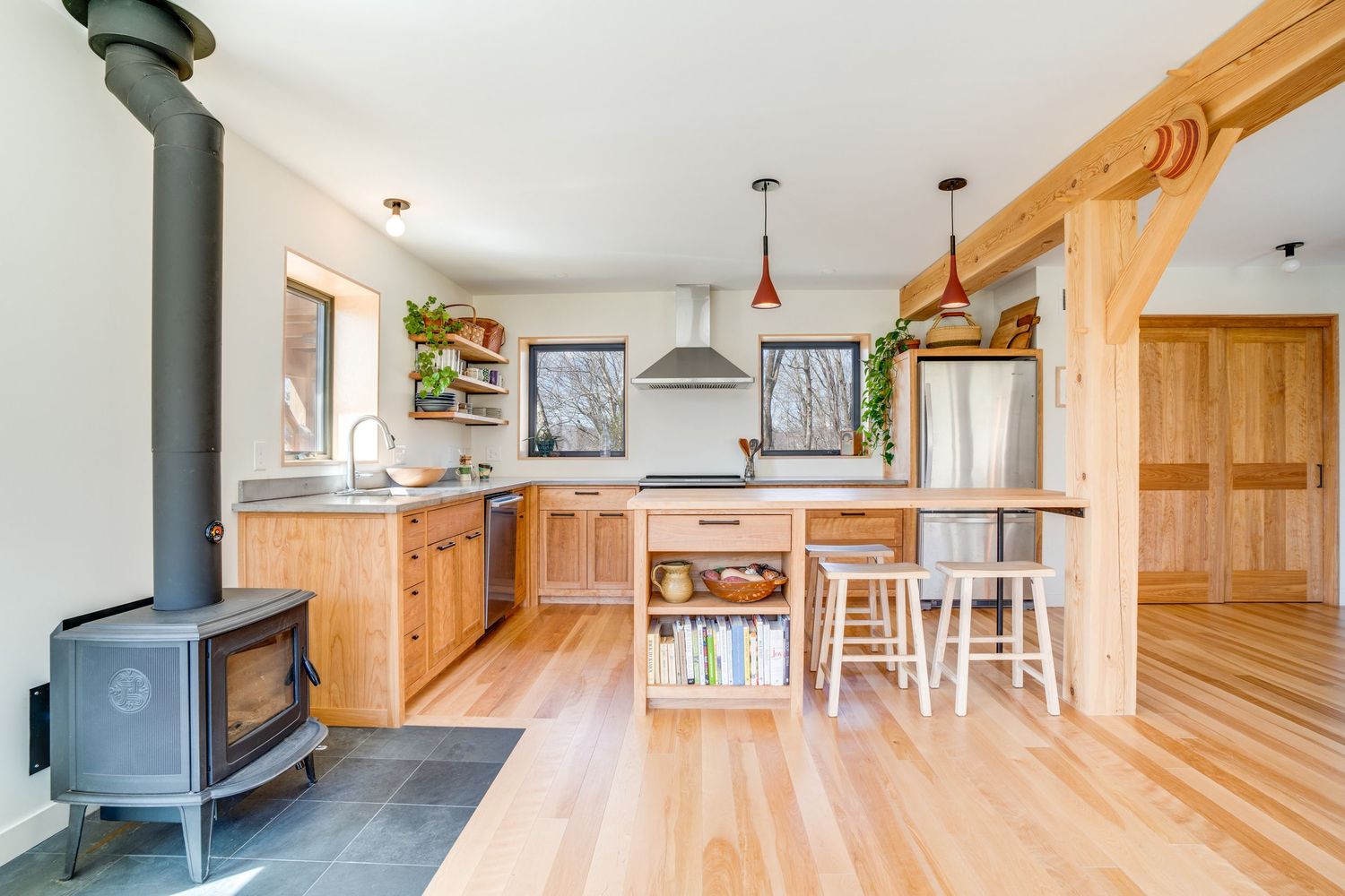 Modern rustic kitchen featuring natural wood cabinets, wood stove, and open layout with pendant lighting and breakfast bar.