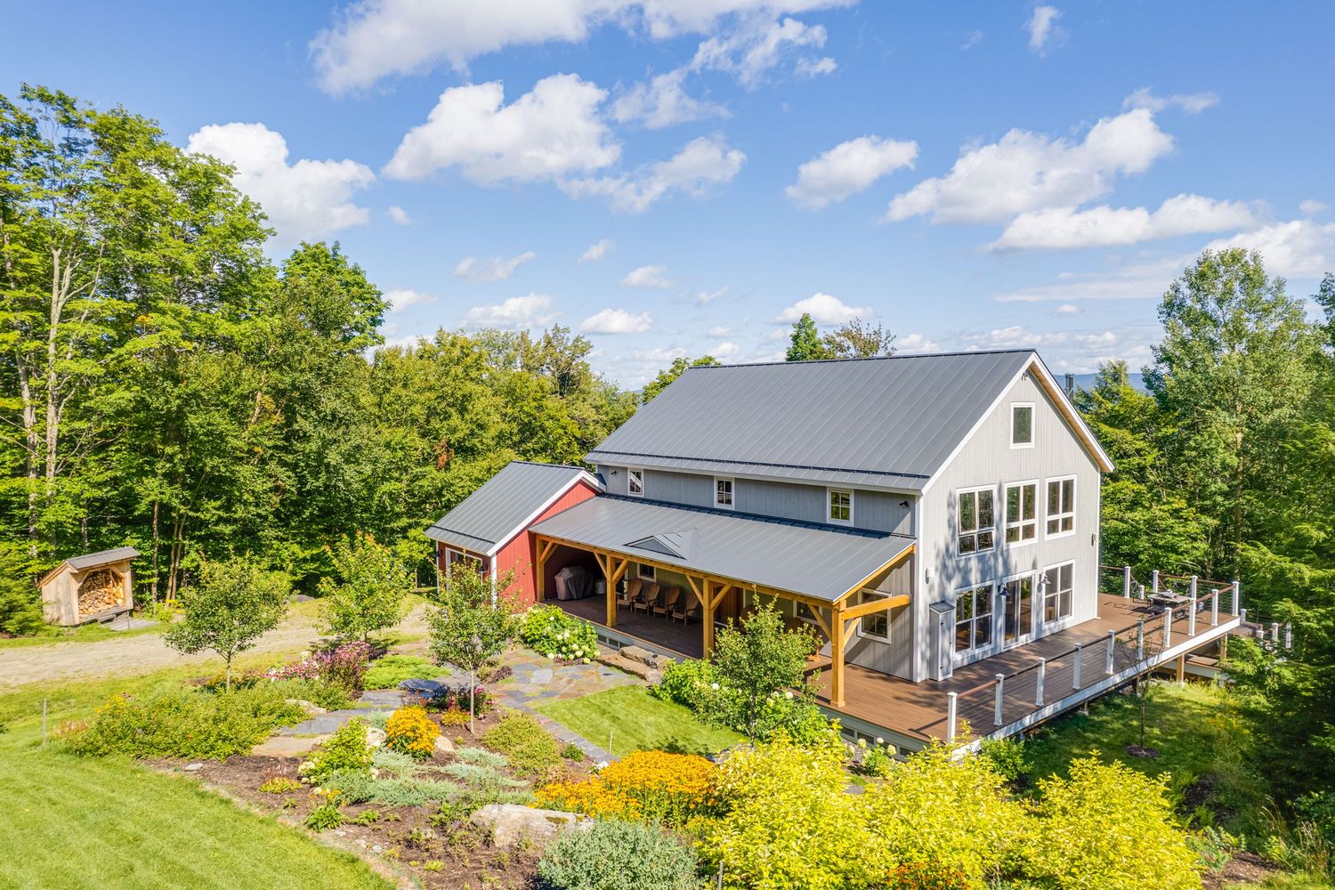 Modern farmhouse exterior with dark metal roof, white siding, and lush landscaping on a sunny day.
