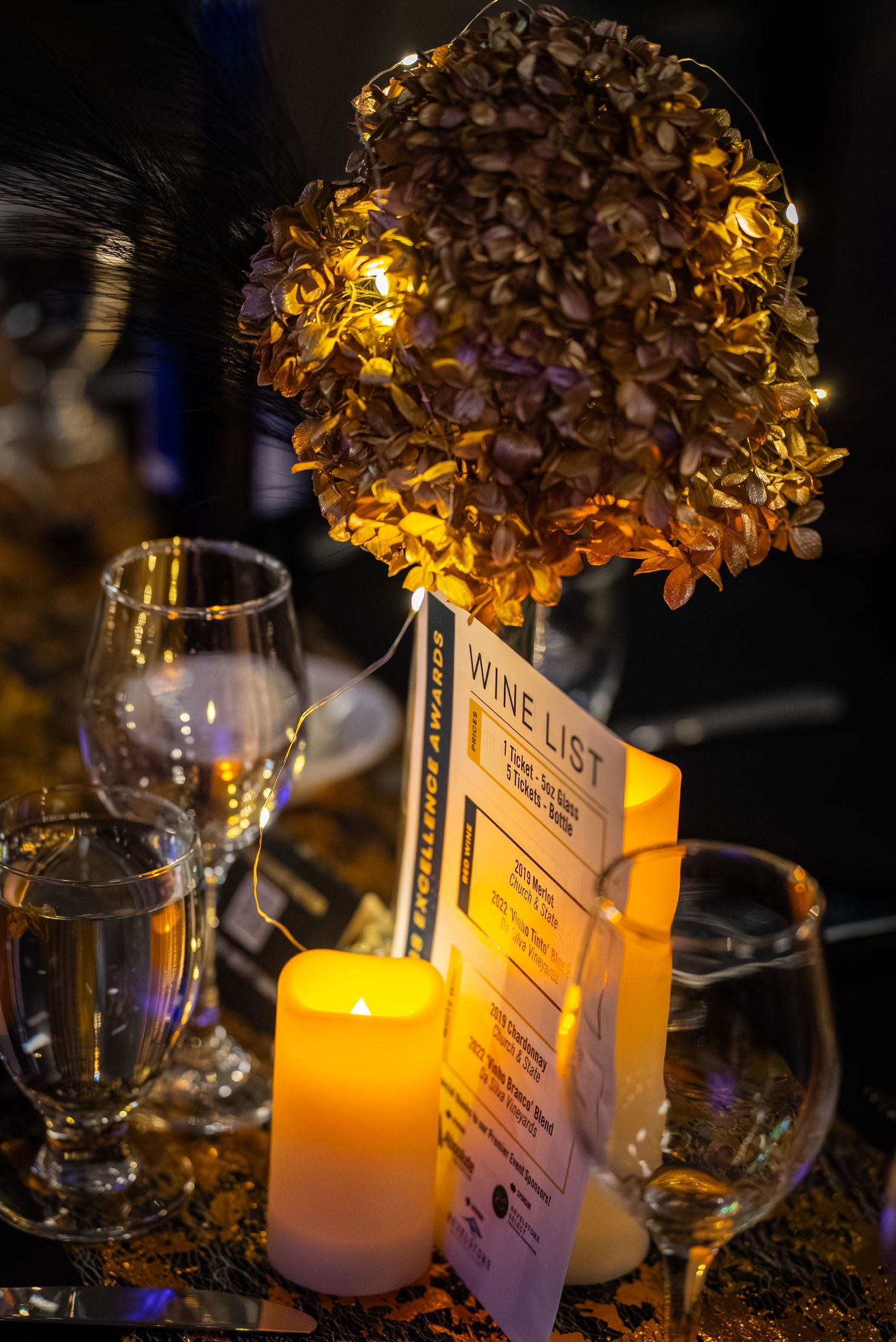 Elegant wedding reception table setting with glowing candles and golden floral centerpieces in dim lighting.