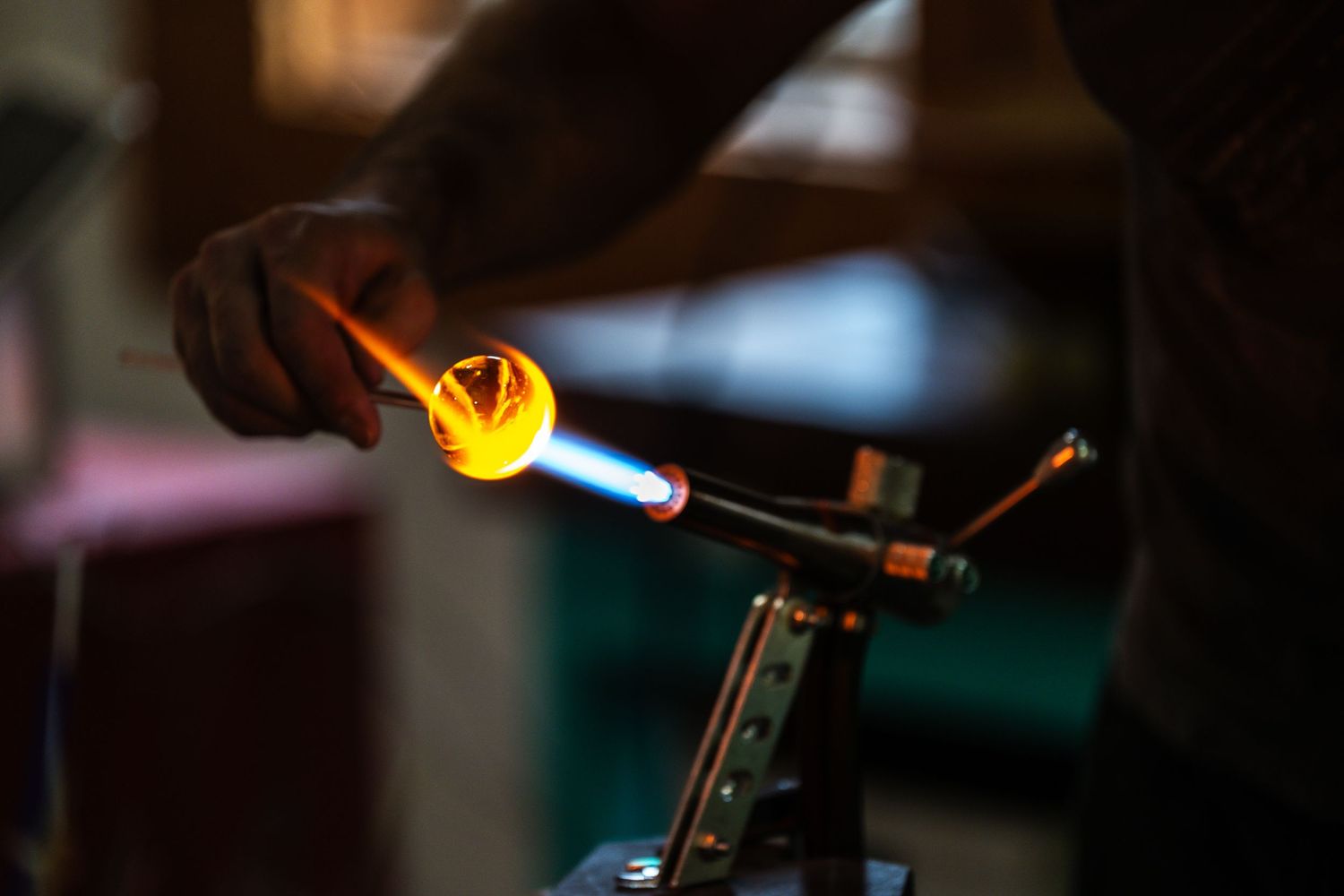 Glass artist uses torch to shape and melt colorful glass tubing in a workshop studio.