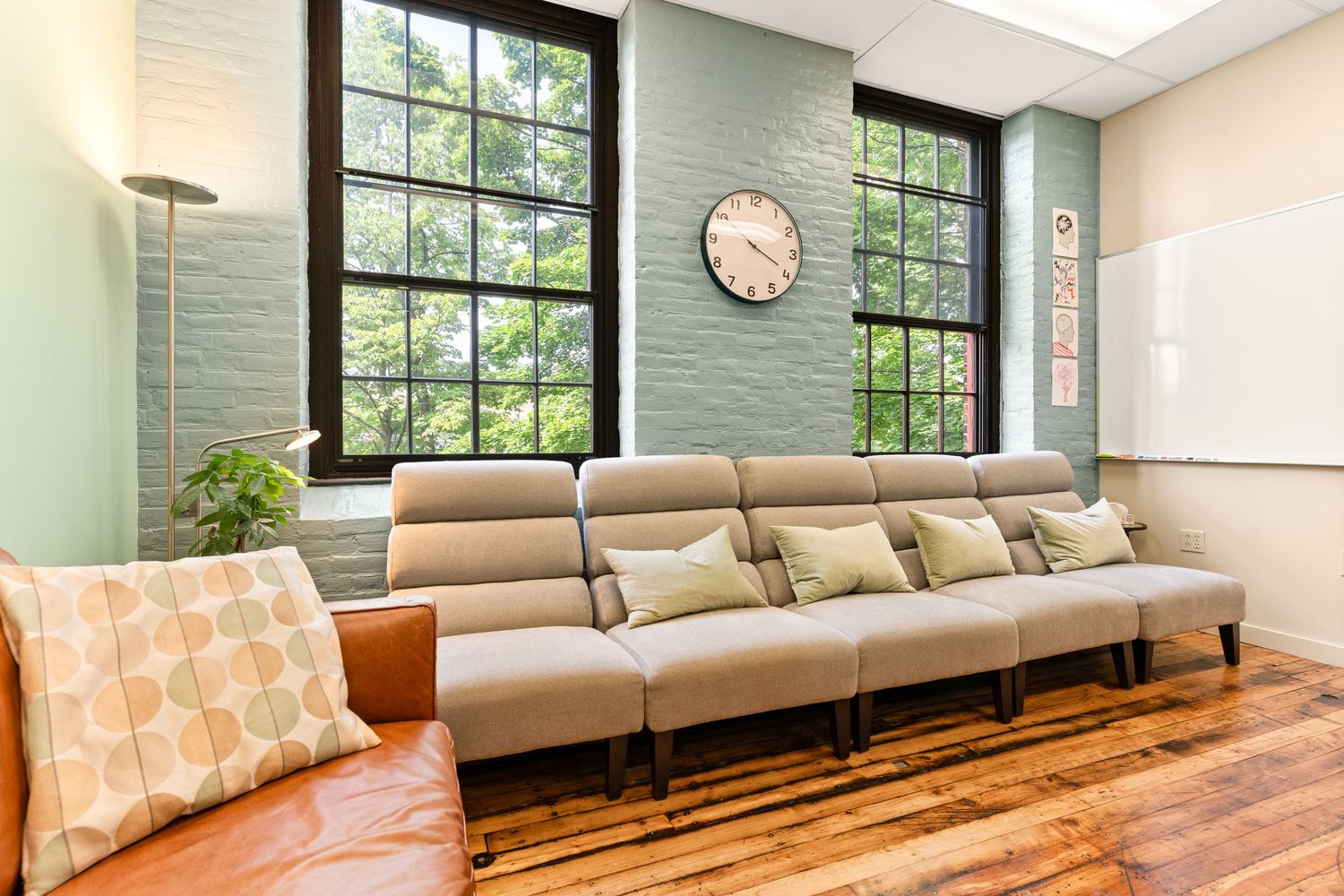 Modern waiting room interior with wooden floors, comfortable seating, and large windows letting in natural light.