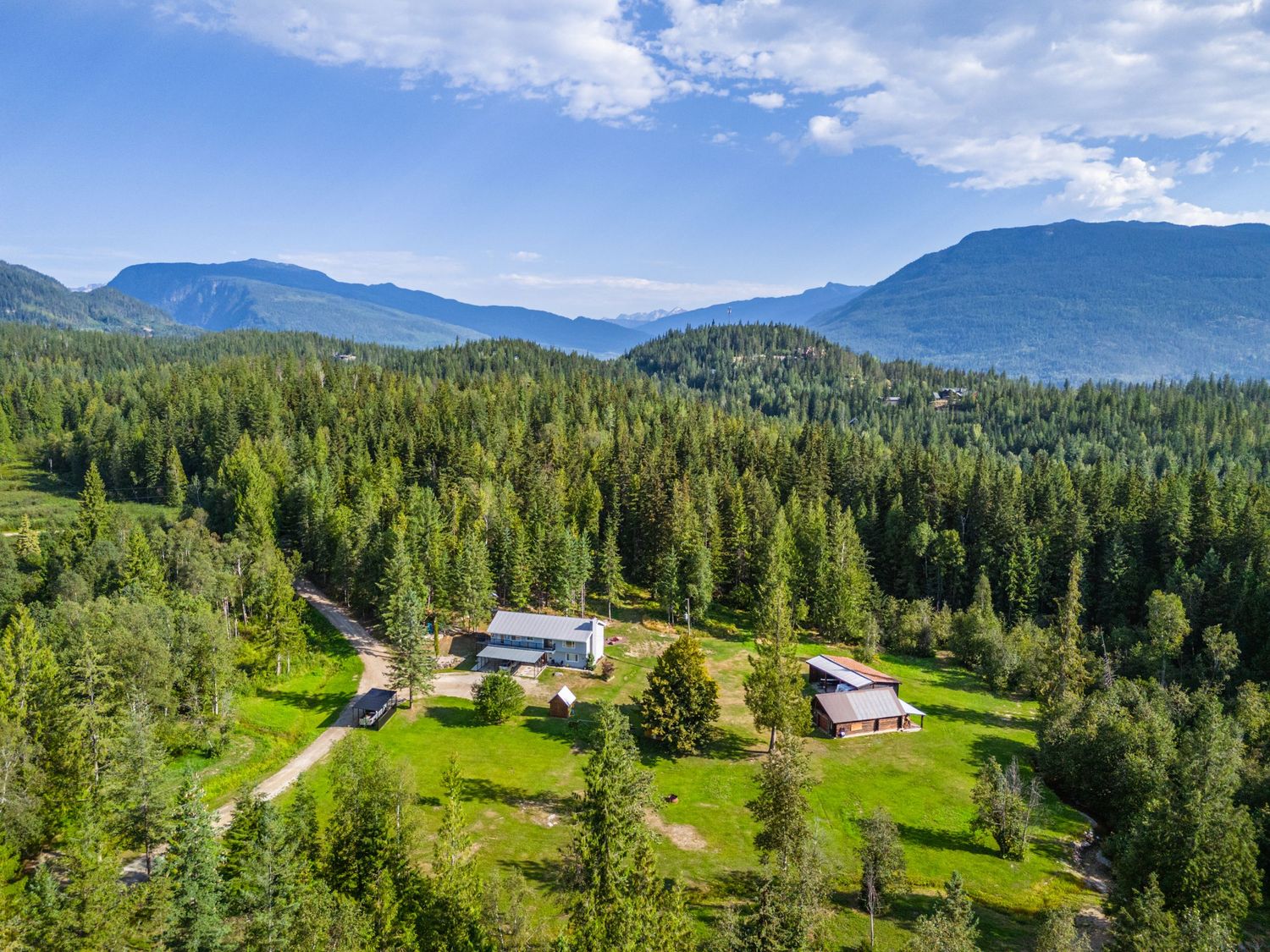 Panoramic mountain landscape with evergreen forests and rural buildings nestled in green valley.