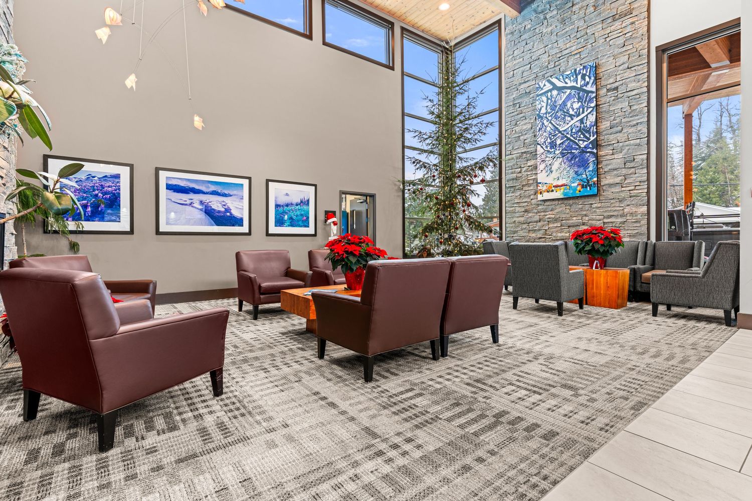 Modern lobby interior with stone accent wall, burgundy leather chairs, and blue artwork displays features vaulted ceiling.
