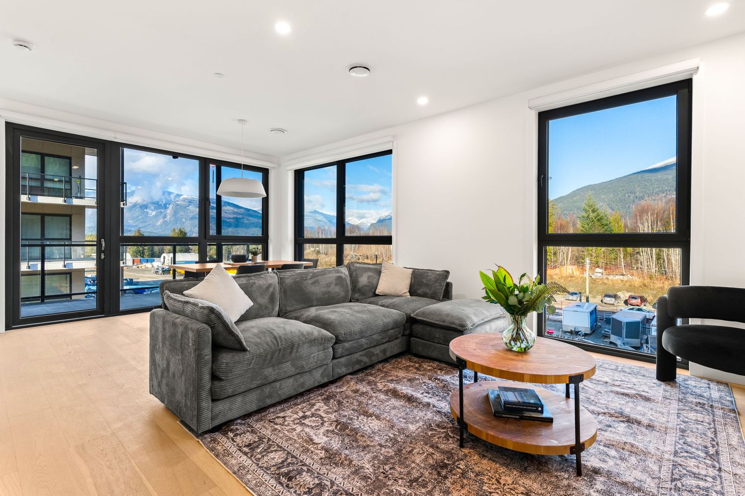 Modern living room with panoramic mountain views features gray sectional sofa and round coffee table on plush area rug.