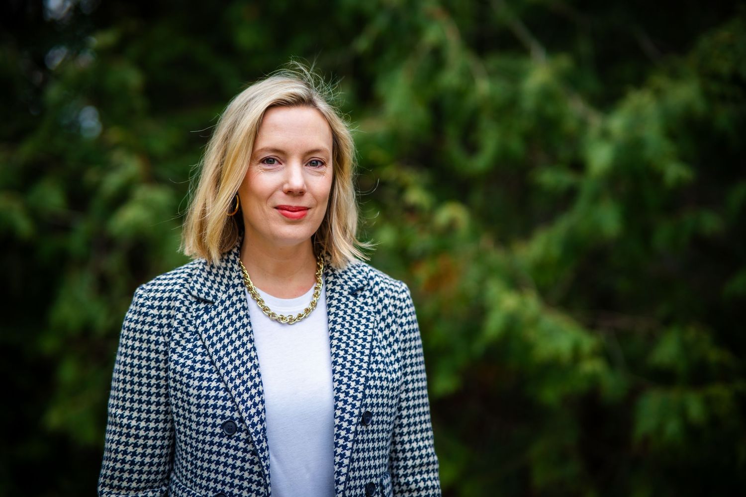 Professional portrait of a person wearing a black and white checkered blazer and white shirt against a blurred green background.