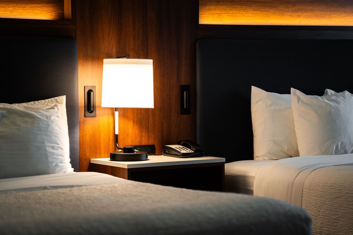 A modern hotel room interior with warm lighting and white bedding illuminated by bedside lamps.