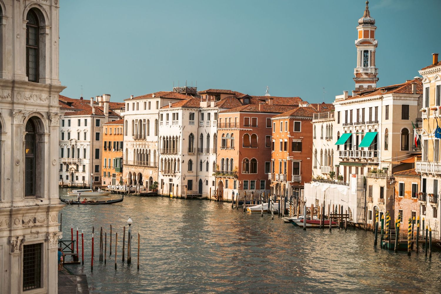 Historic buildings and palaces line the Grand Canal in Venice, Italy with traditional wooden mooring poles in the water.