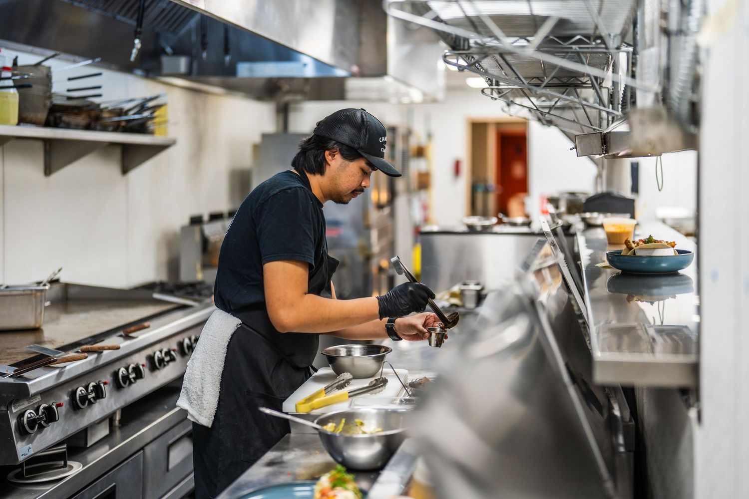 Busy restaurant kitchen with chefs preparing food at stainless steel workstations.
