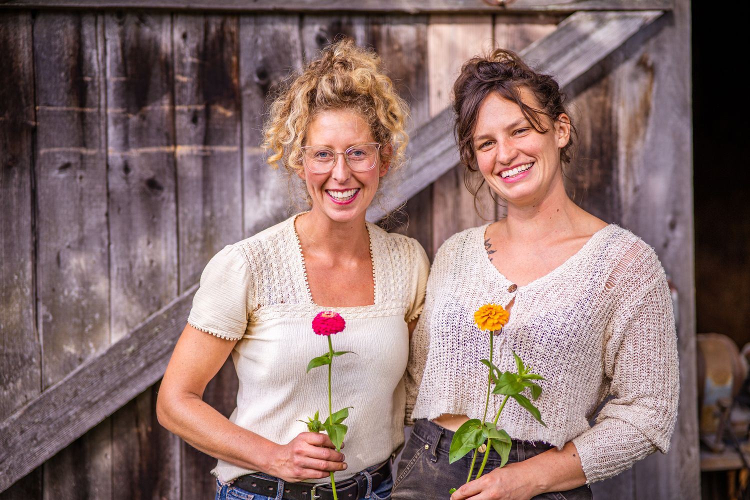 Two people laughing and holding flowers while sitting together on rustic wooden steps.