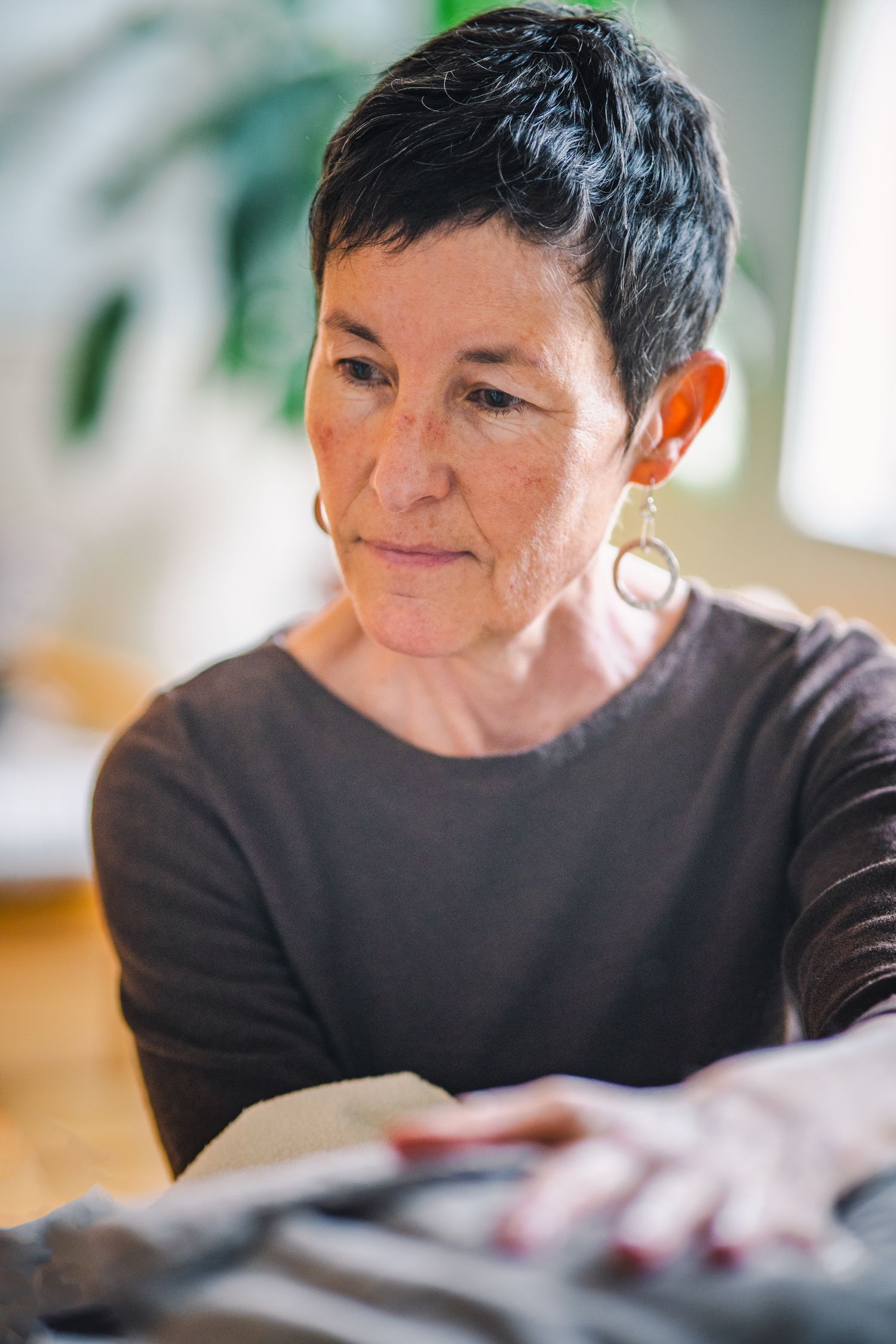 A person with short dark hair wearing a brown sweater sits at a table while looking down at something.