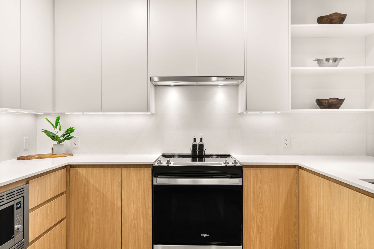 Modern U-shaped kitchen with light wood lower cabinets, white upper cabinets, and sleek stainless steel appliances.