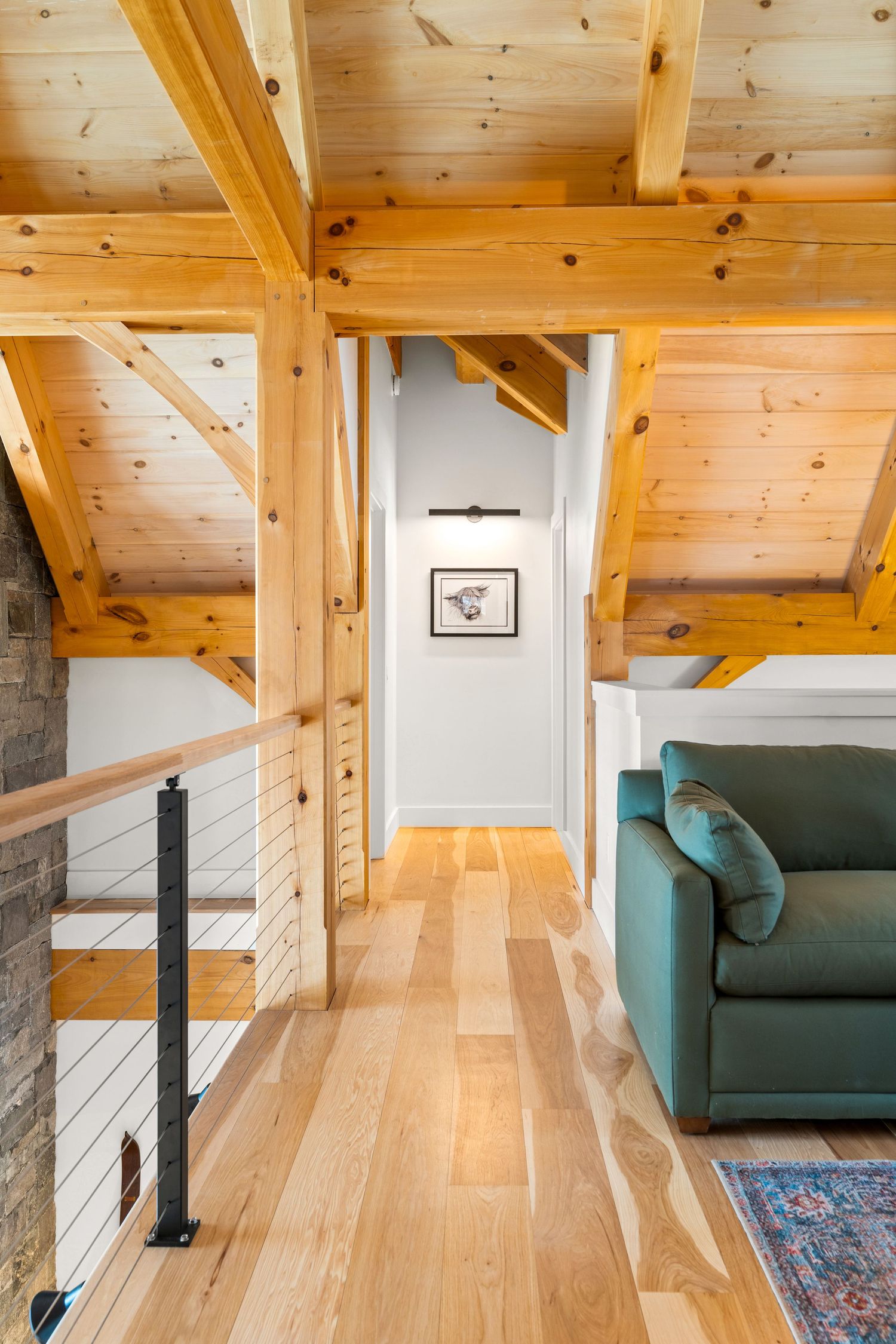 Modern timber-frame loft space with exposed beams, hardwood floors, and a teal accent chair.