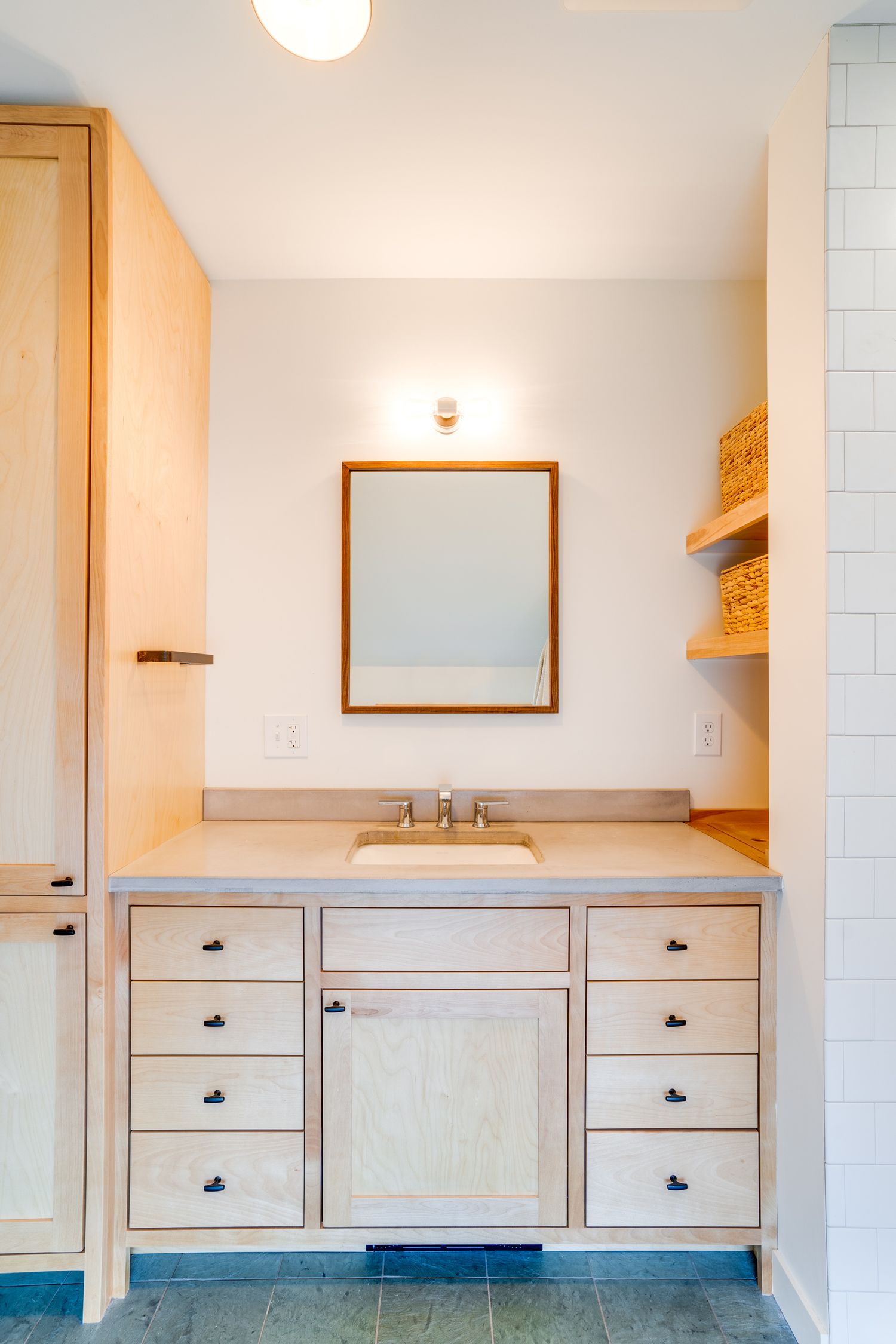 Clean and minimal bathroom vanity with wooden cabinetry, framed mirror, and stone countertop.