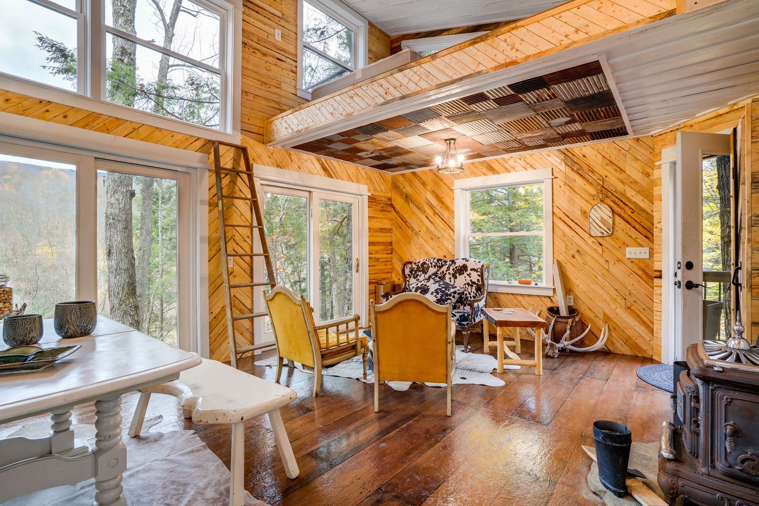 Rustic living area with wood paneling, large windows, exposed beams, and mountain views.
