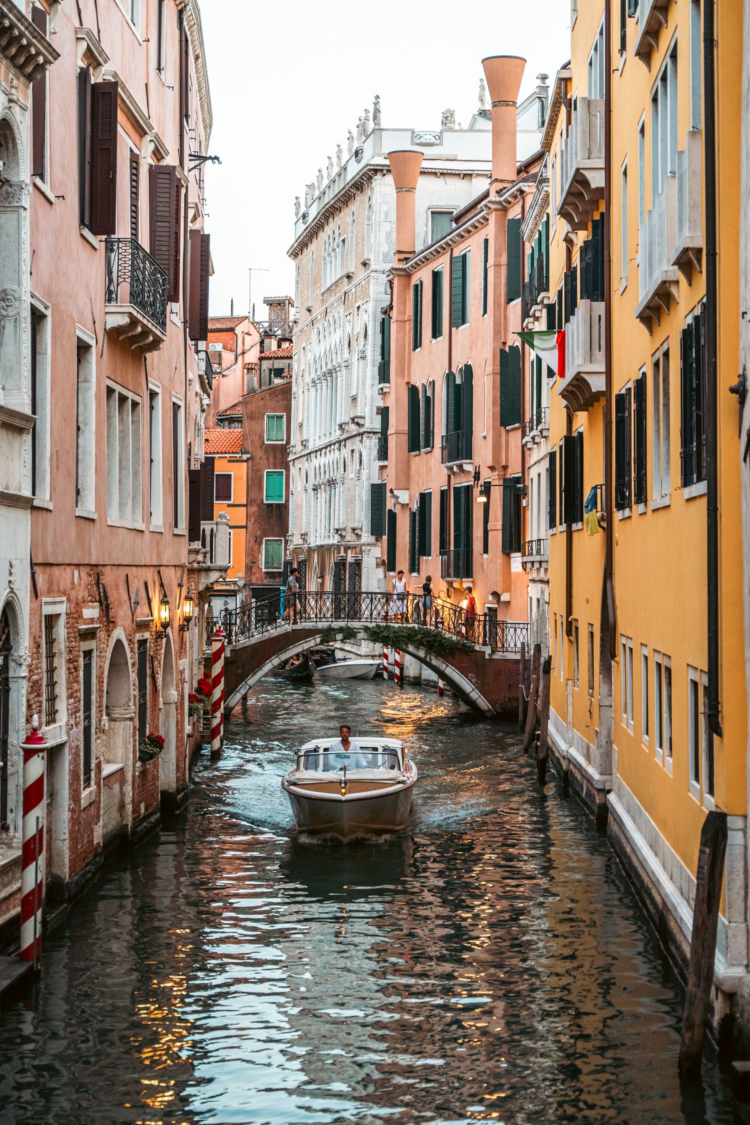 Narrow canals of Venice with colorful buildings and traditional boats reflecting in dark waters during evening light.