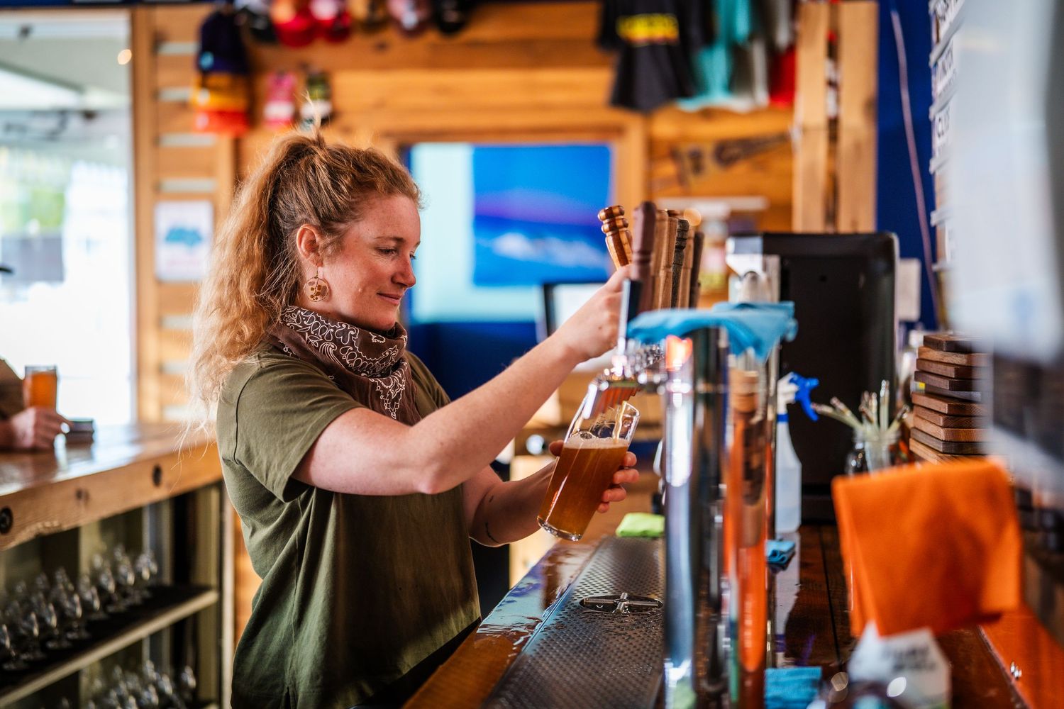 People enjoying drinks at a rustic wooden bar counter with bottles and glassware visible.