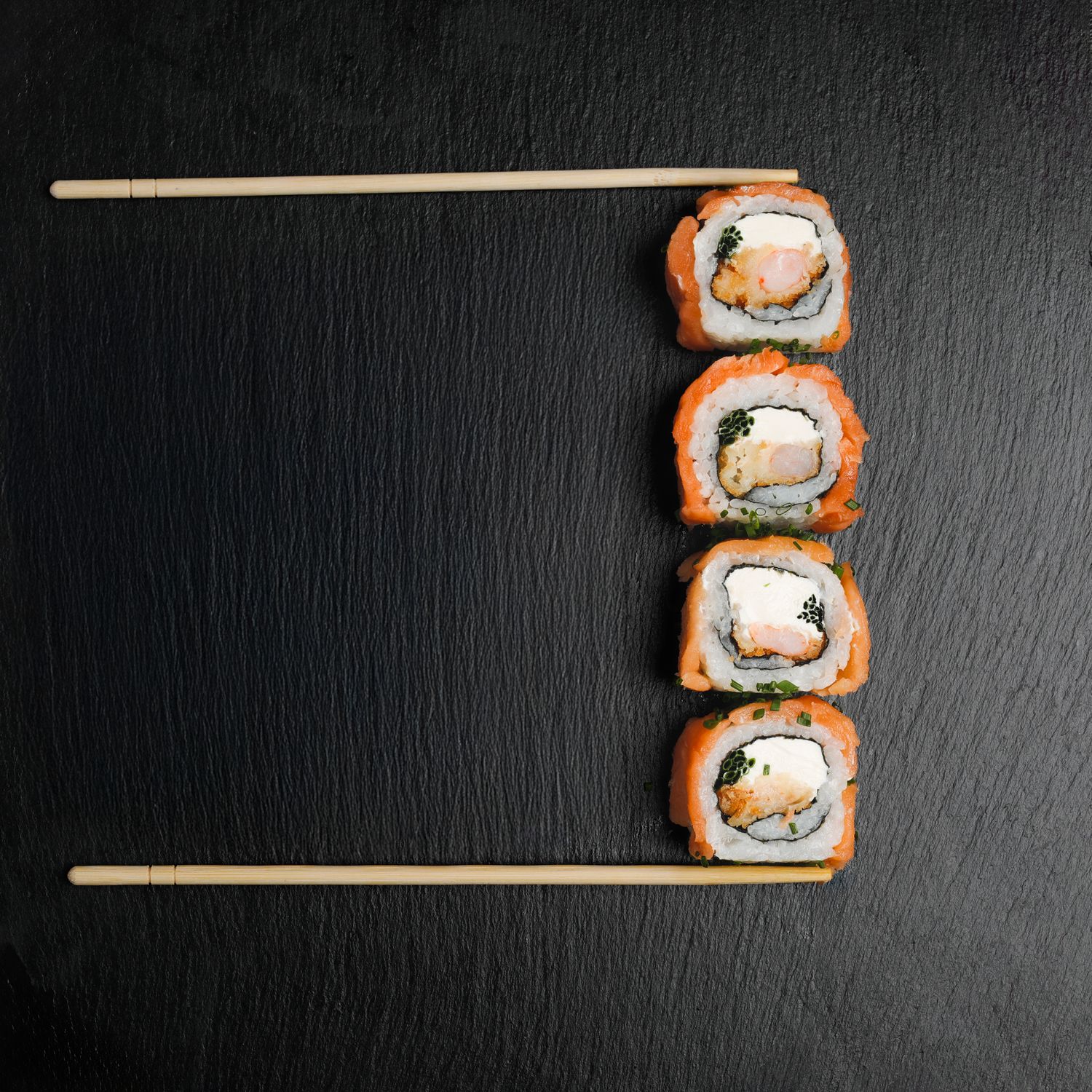 Sushi alineado con palillos sobre fondo negro, fotografía de producto gastronómico.