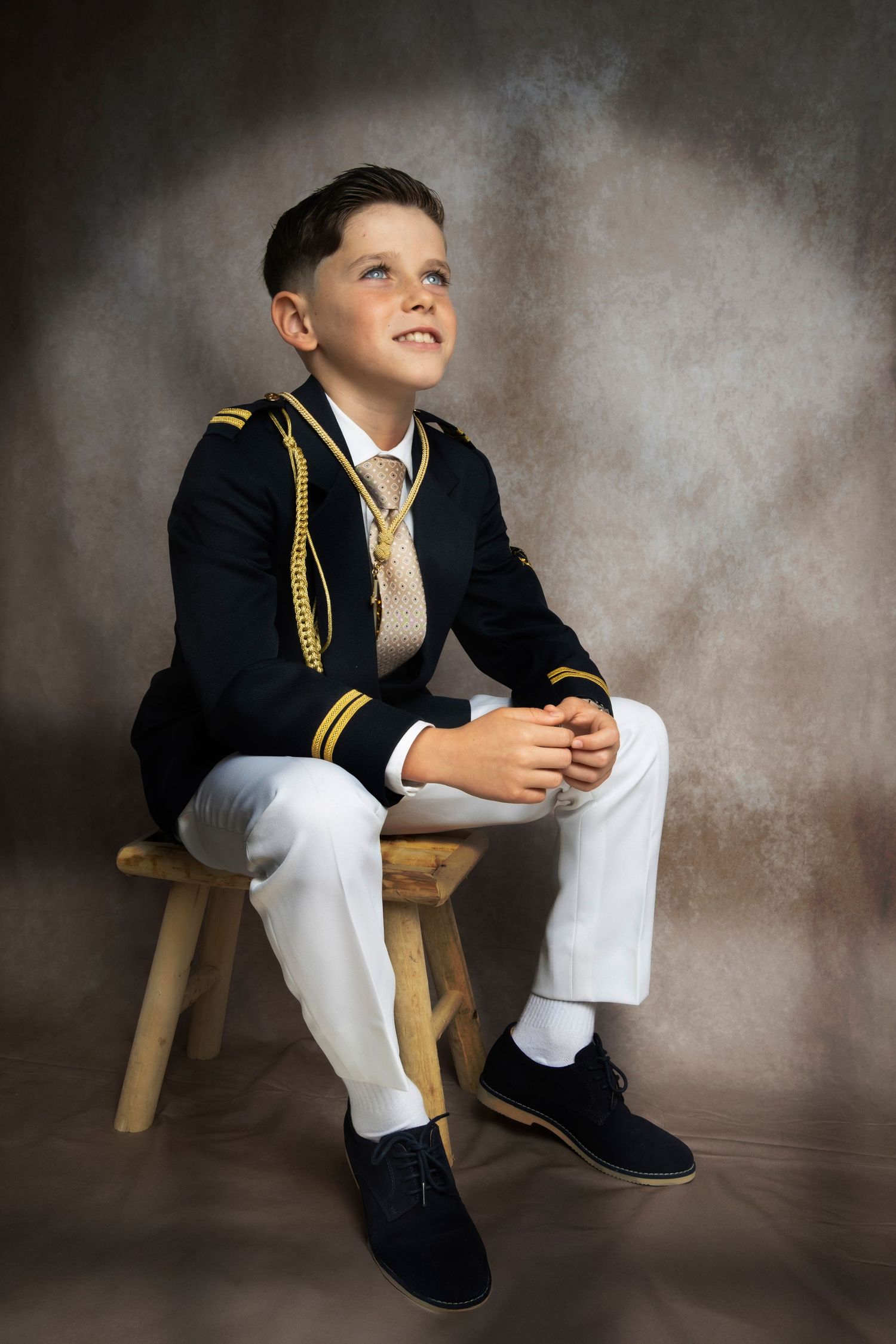Retrato de primera comunión en estudio fotográfico profesional en Oviedo. Fotografía elegante y atemporal de niño con traje de comunión sobr