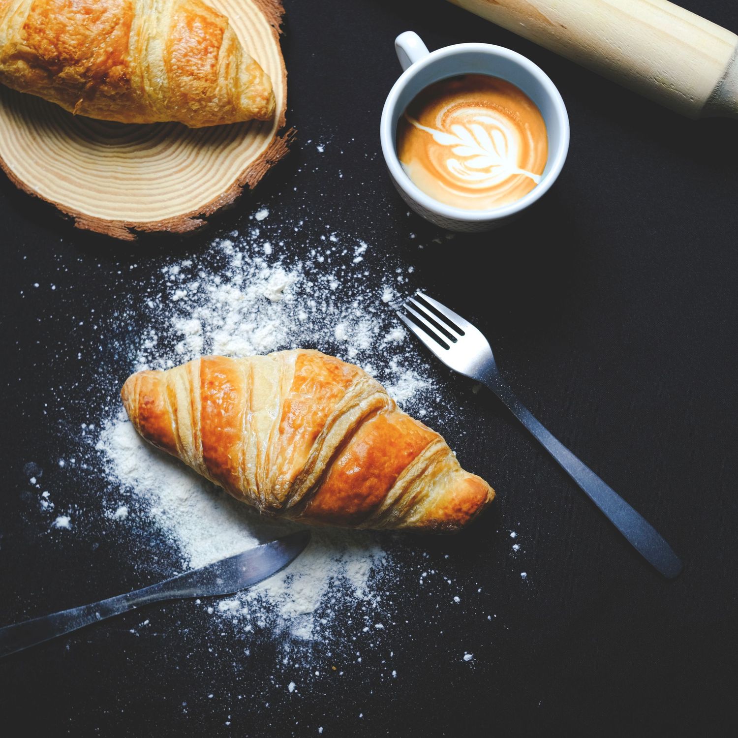 Fotografía gastronómica de croissant con café en mesa oscura, imagen profesional para cafetería o brunch.