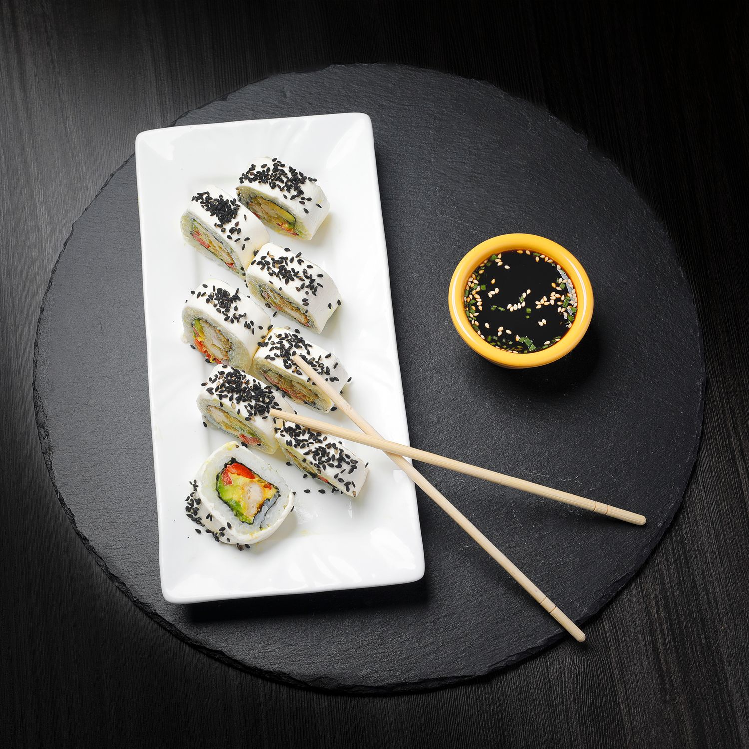 Sushi gourmet en plato negro con palillos, fotografía gastronómica minimalista de cocina japonesa.