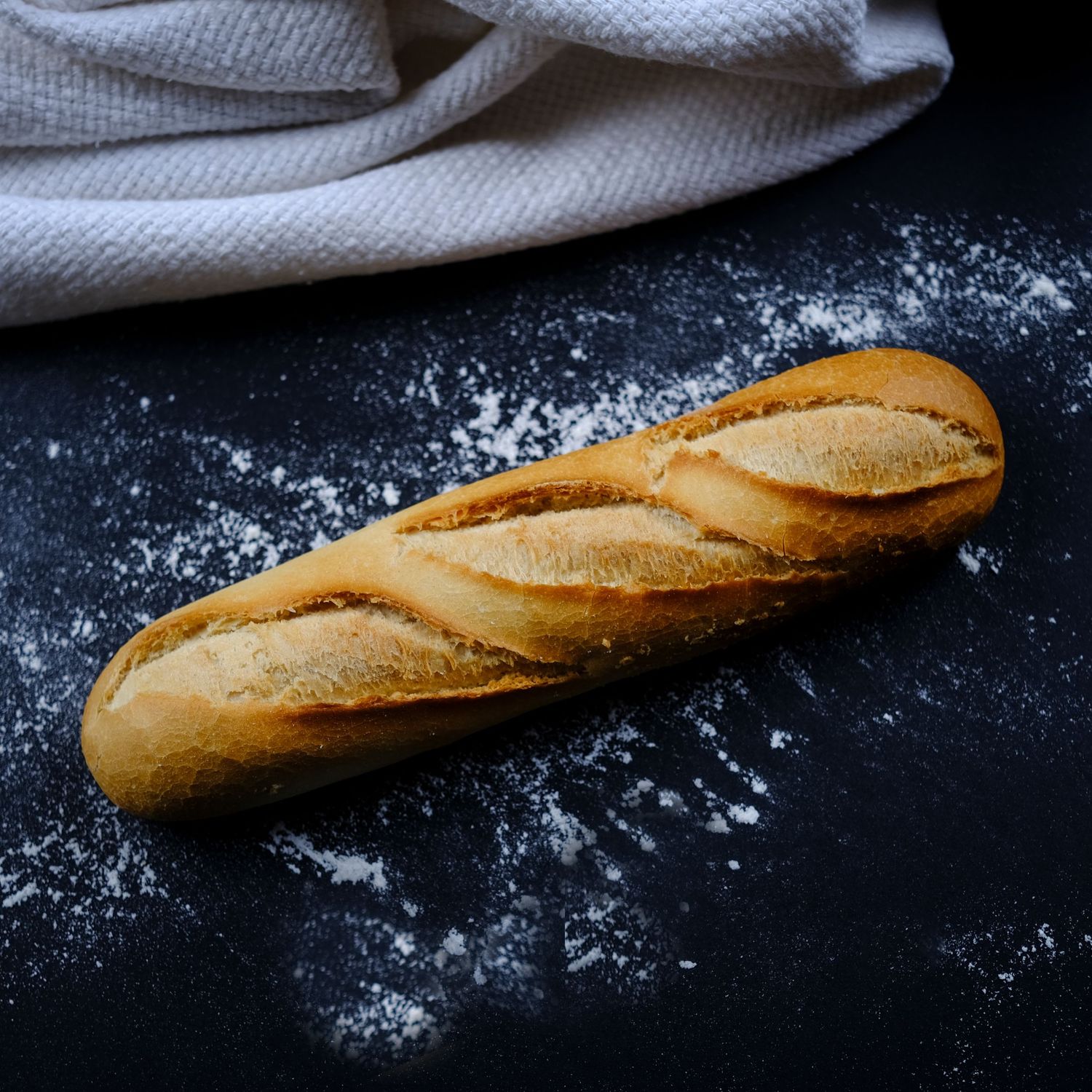 Fotografía gastronómica de baguette artesanal sobre mesa con harina, imagen profesional de panadería.