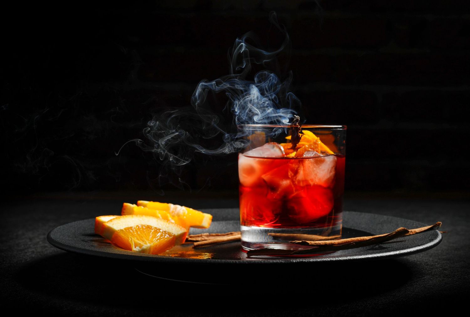 Cóctel ahumado con hielo y cítricos, fotografía artística de bebida.