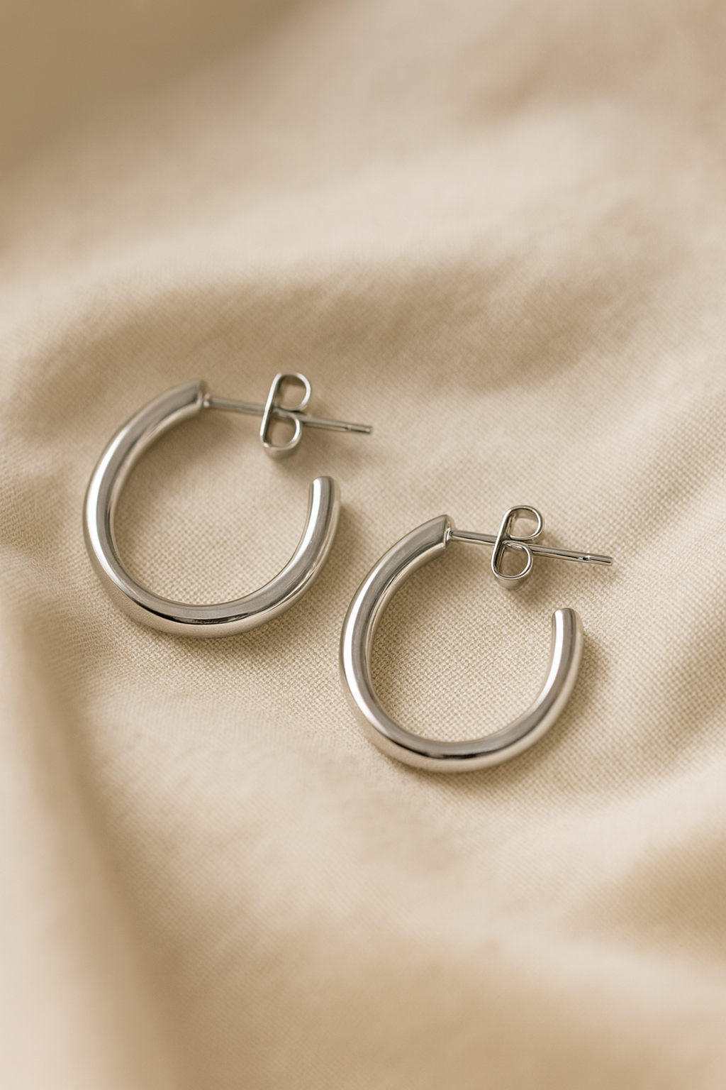 Fotografía artística de pendientes dorados sobre tela beige. Imagen cálida y elegante para catálogo de joyas premium.