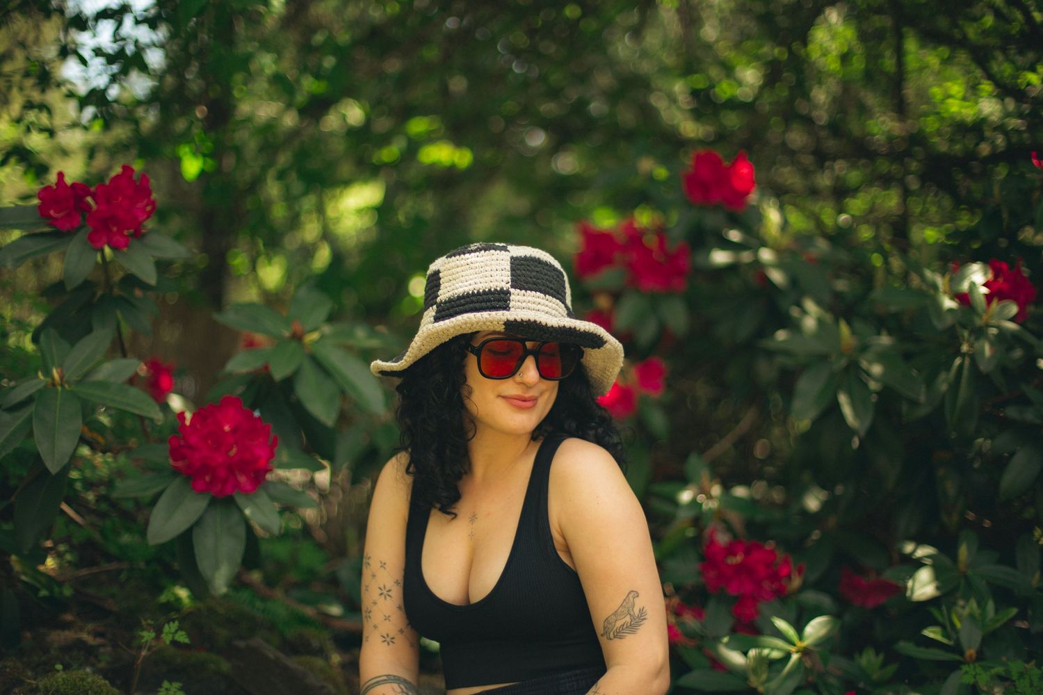 Portrait of a woman with black curly hair with red flowers behind her in a forested background.