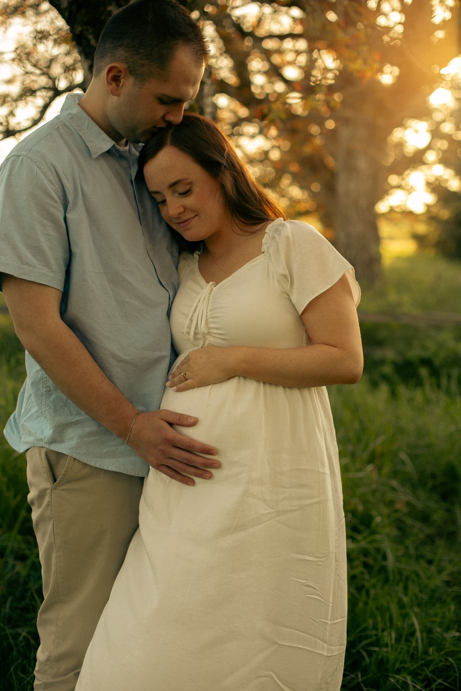 A couple embrace while the man's hand is on his wife's pregnant belly for a maternity photoshoot