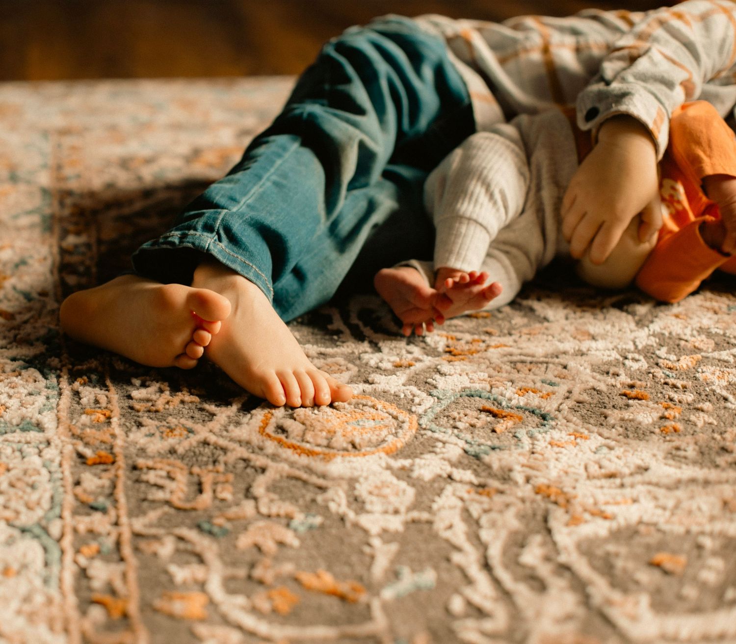A brother and his baby sister cuddling on the carpet for a family new-born photoshoot.
