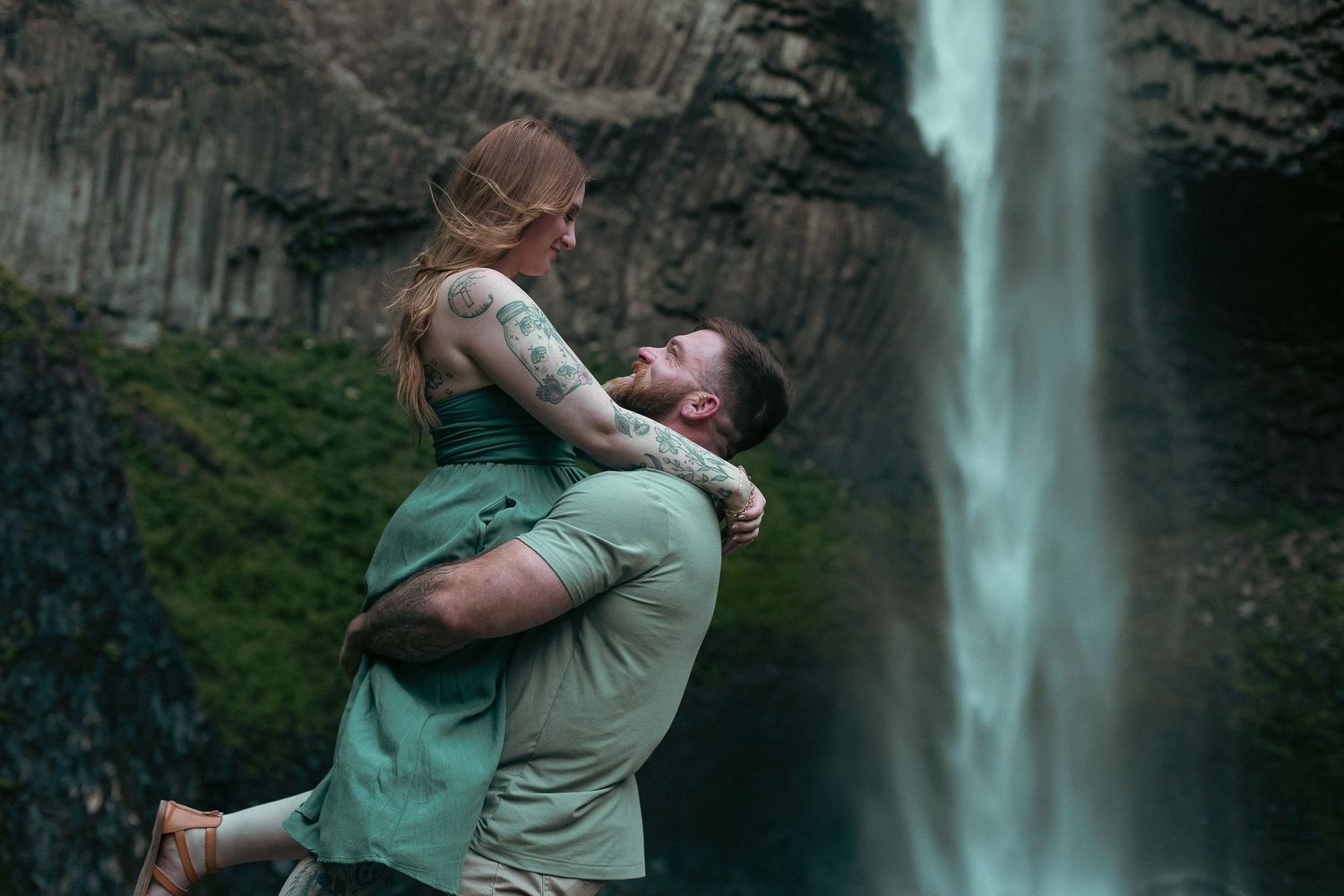 A man picking up his fiancé in front of an Oregon waterfall for an engagement photoshoot
