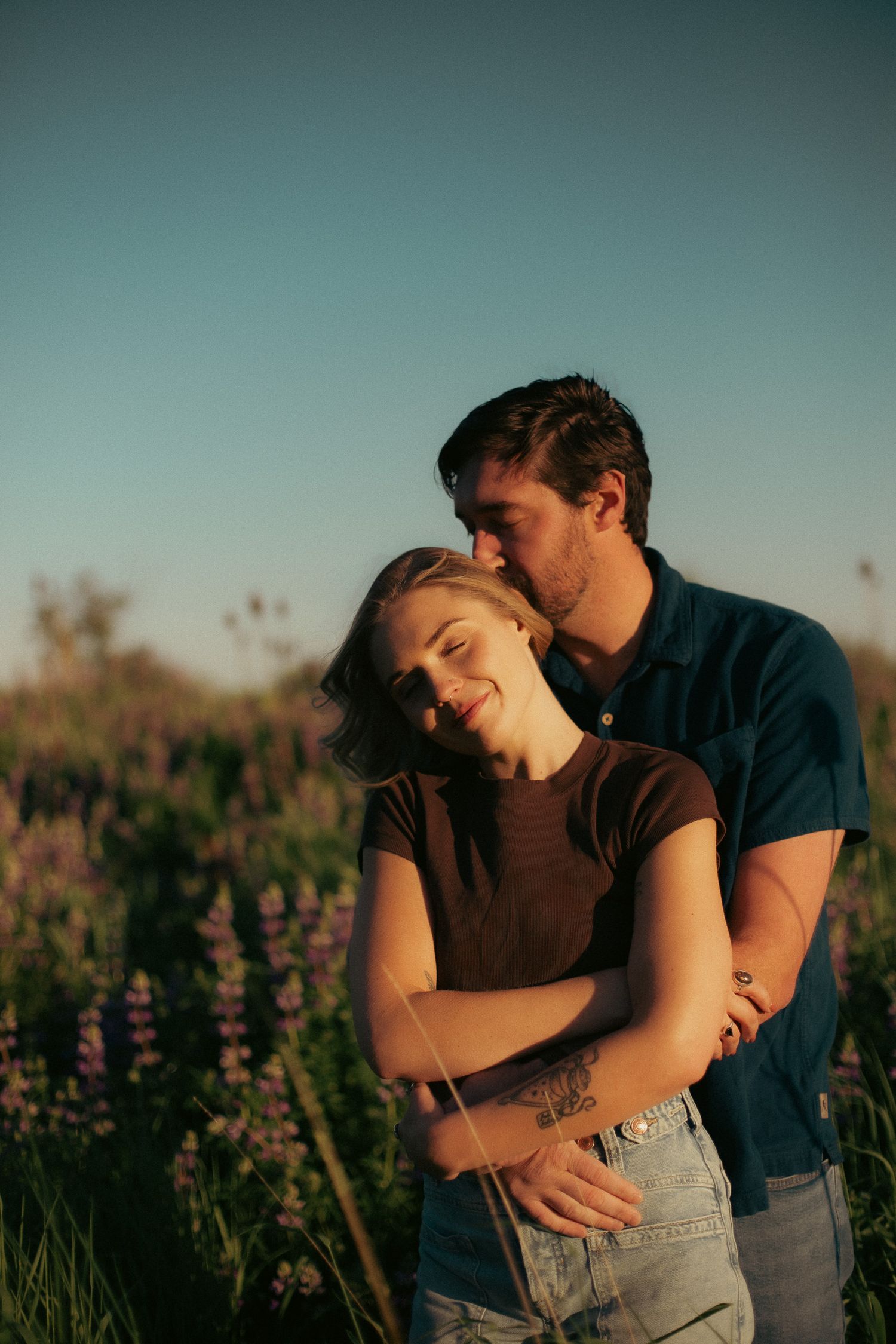A couple embraces in front of lupine flowers in a sunset-lit field for engagement photos in Portland, Oregon