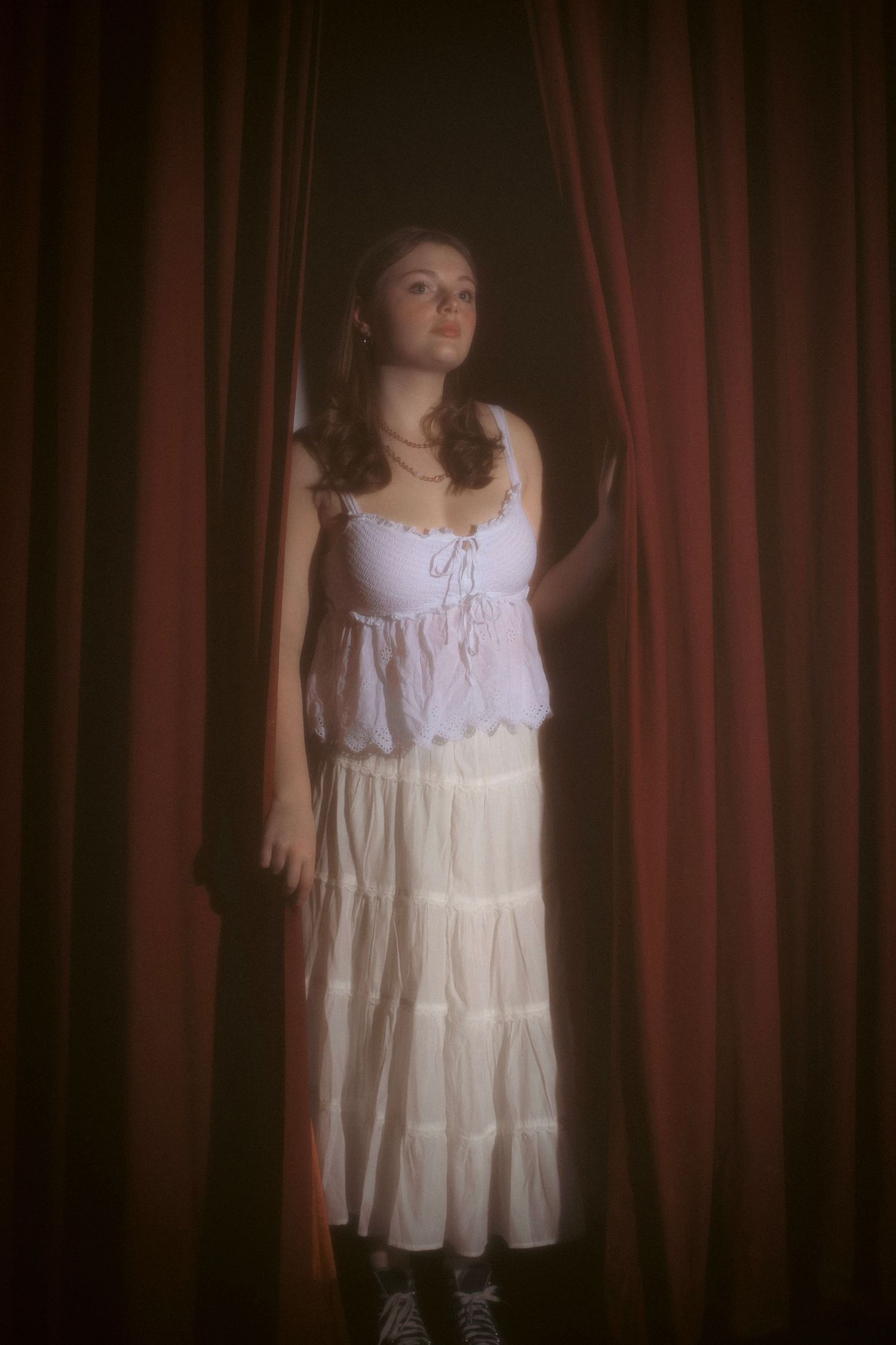 young woman in a vintage theater peeking through the stage curtain