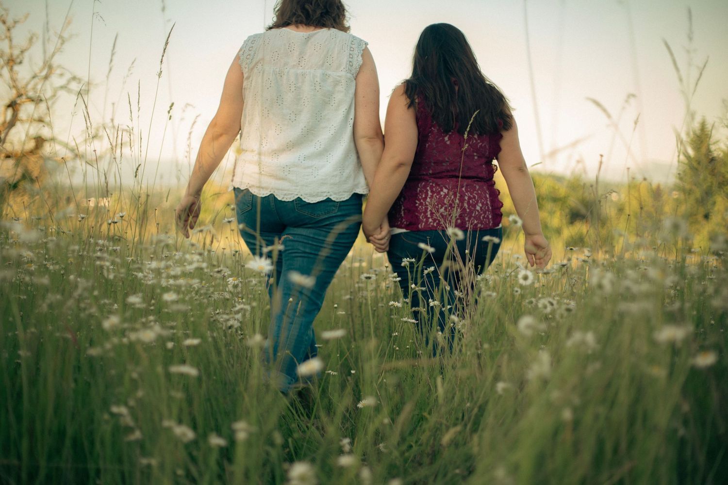 Two women holding hands and walking through a field of white flowers.