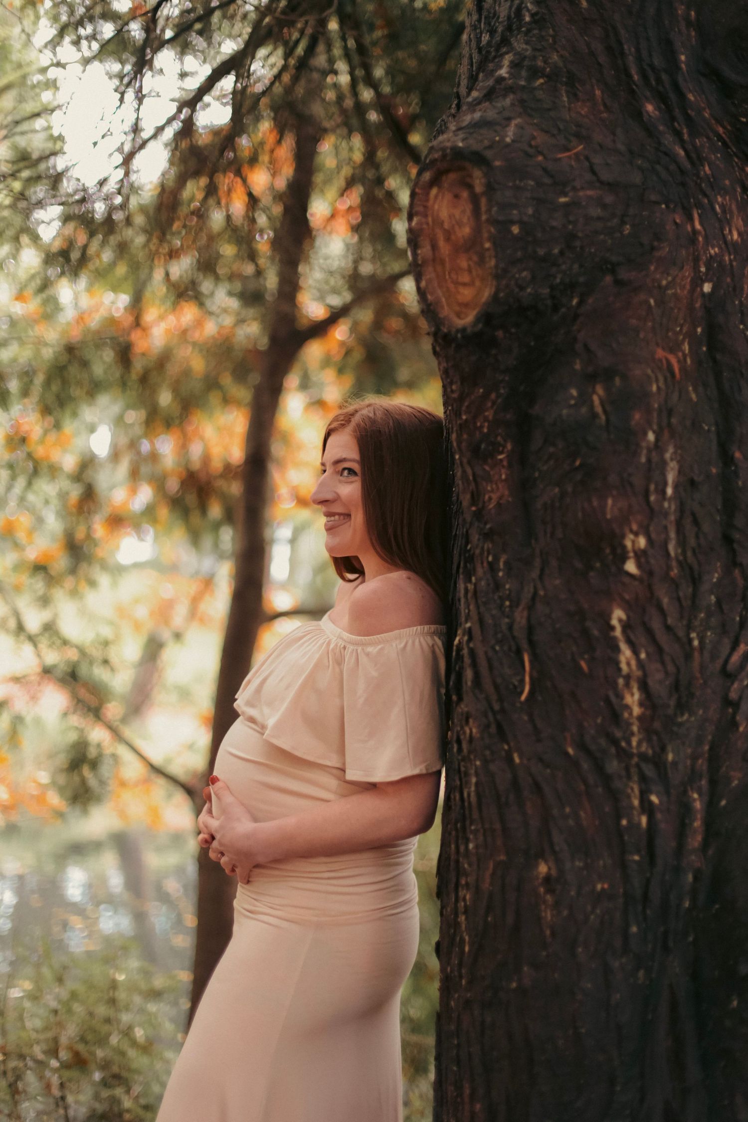 woman posing in a pink dress against a tree for a maternity photoshoot