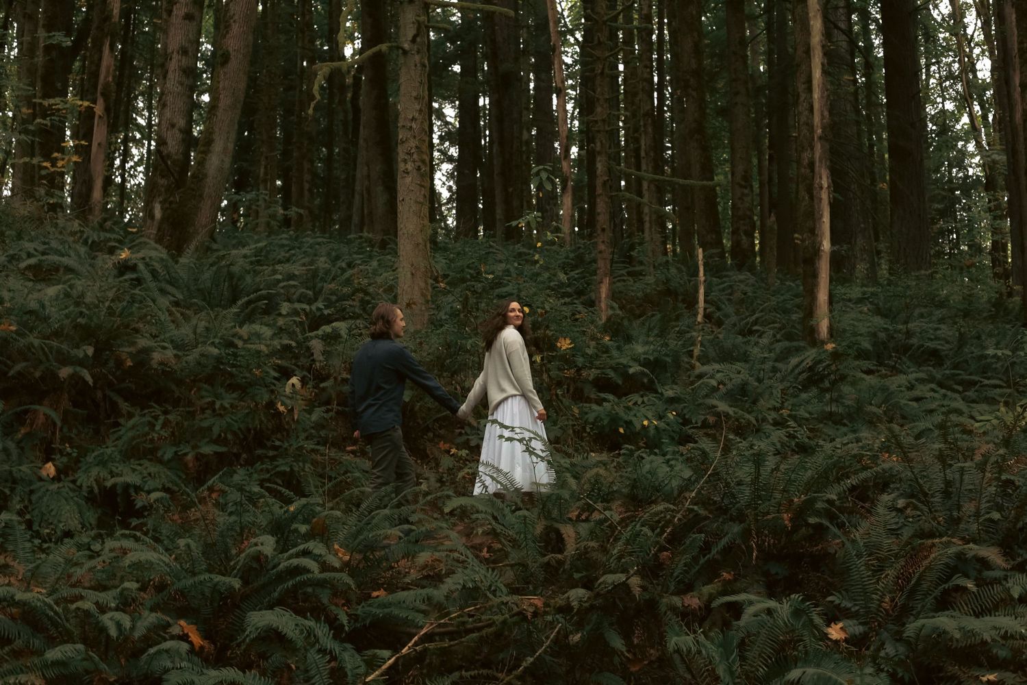 A young newly married couple walk hand-in-hand amongst a moody, green, lush forest backdrop for an elopement photoshoot in Portland, OR