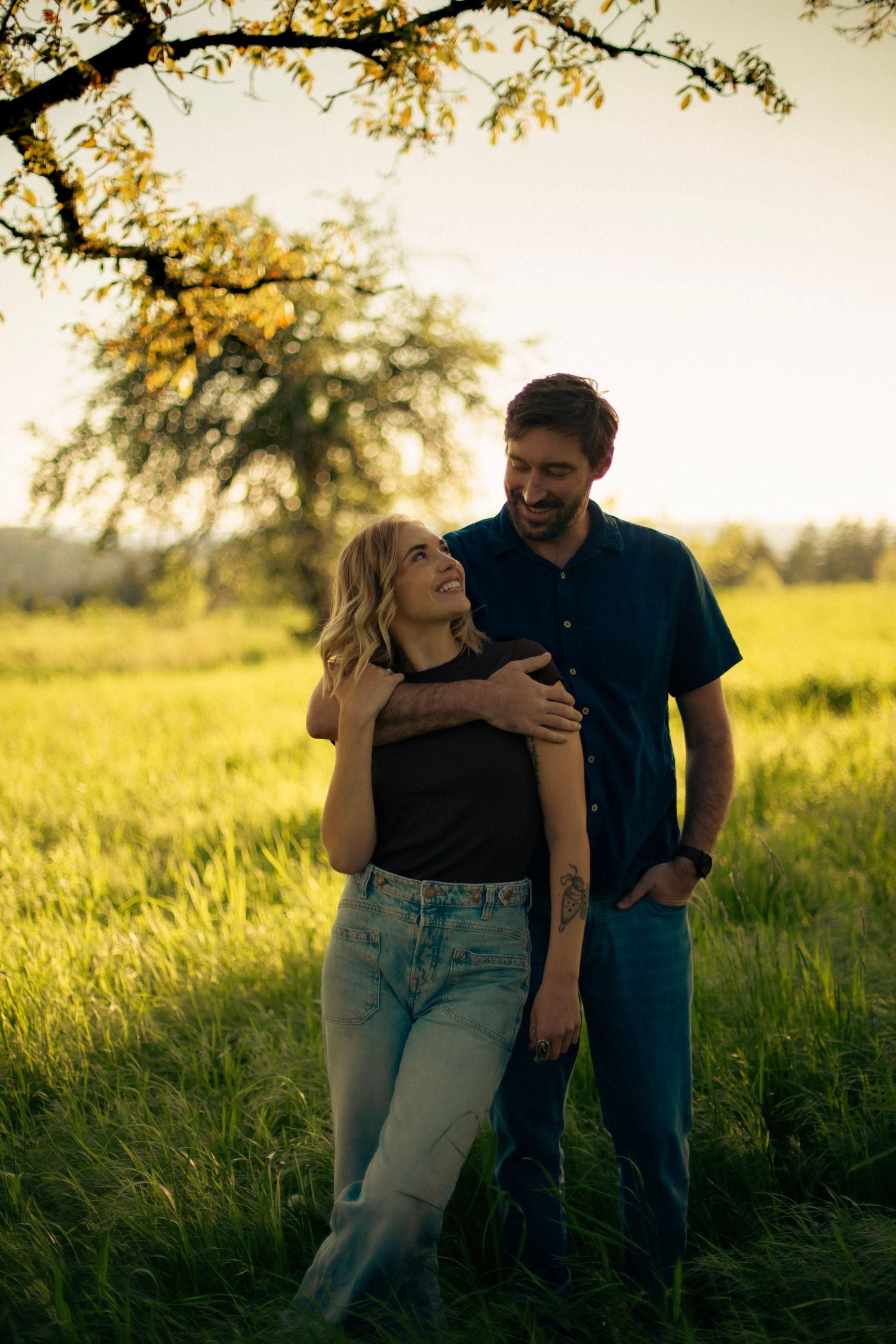 A couple posing and laughing together in a field at sunset