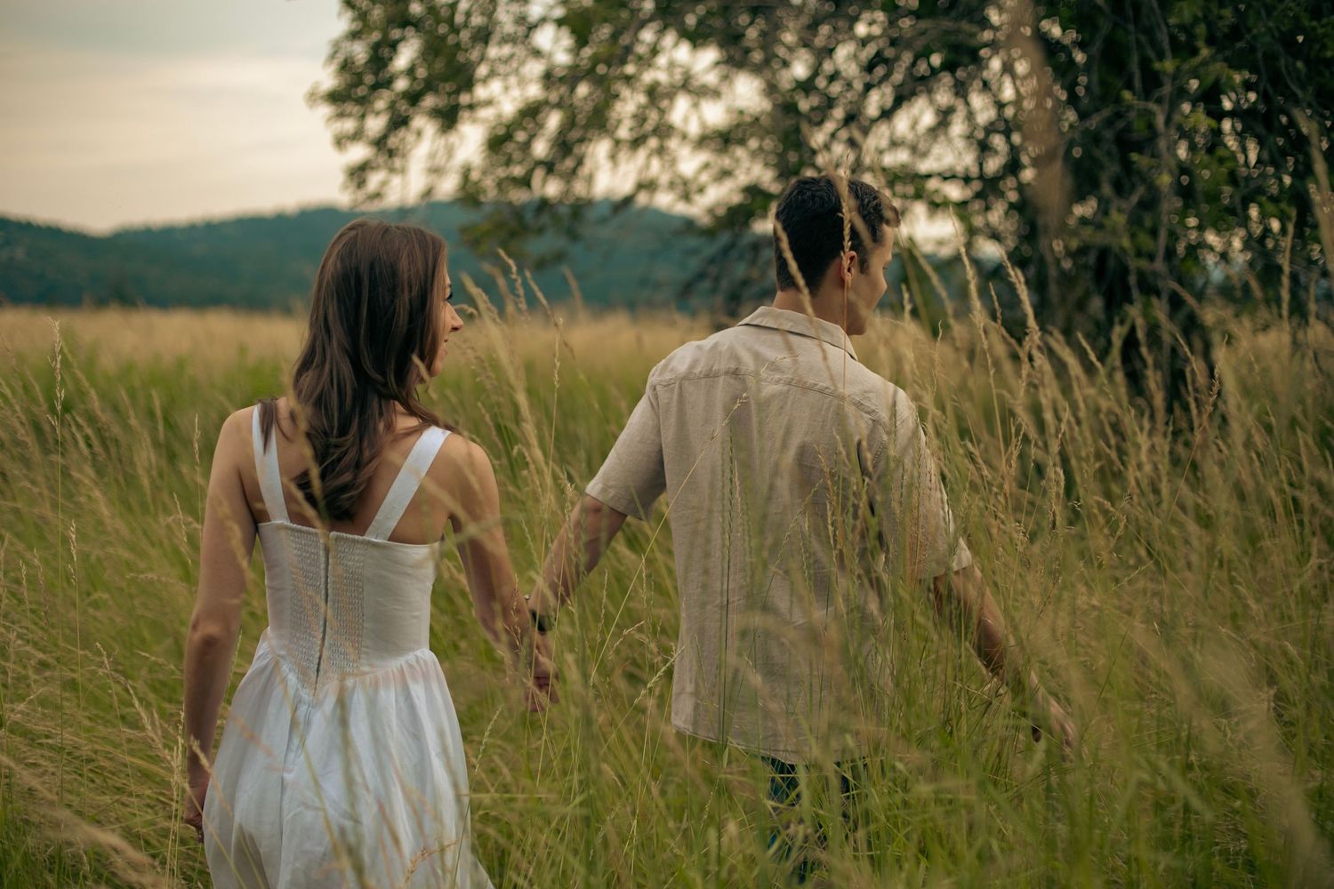 A man and woman holding hands while the man leads the woman through a field of tall grass