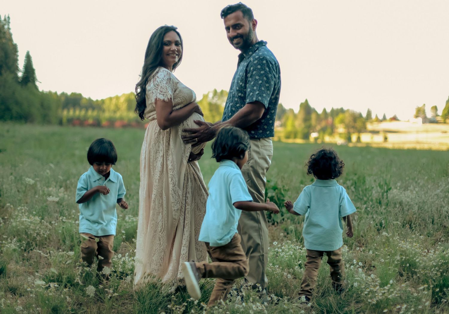 Three young boys run in circles around their parents in a green, wildflower field.