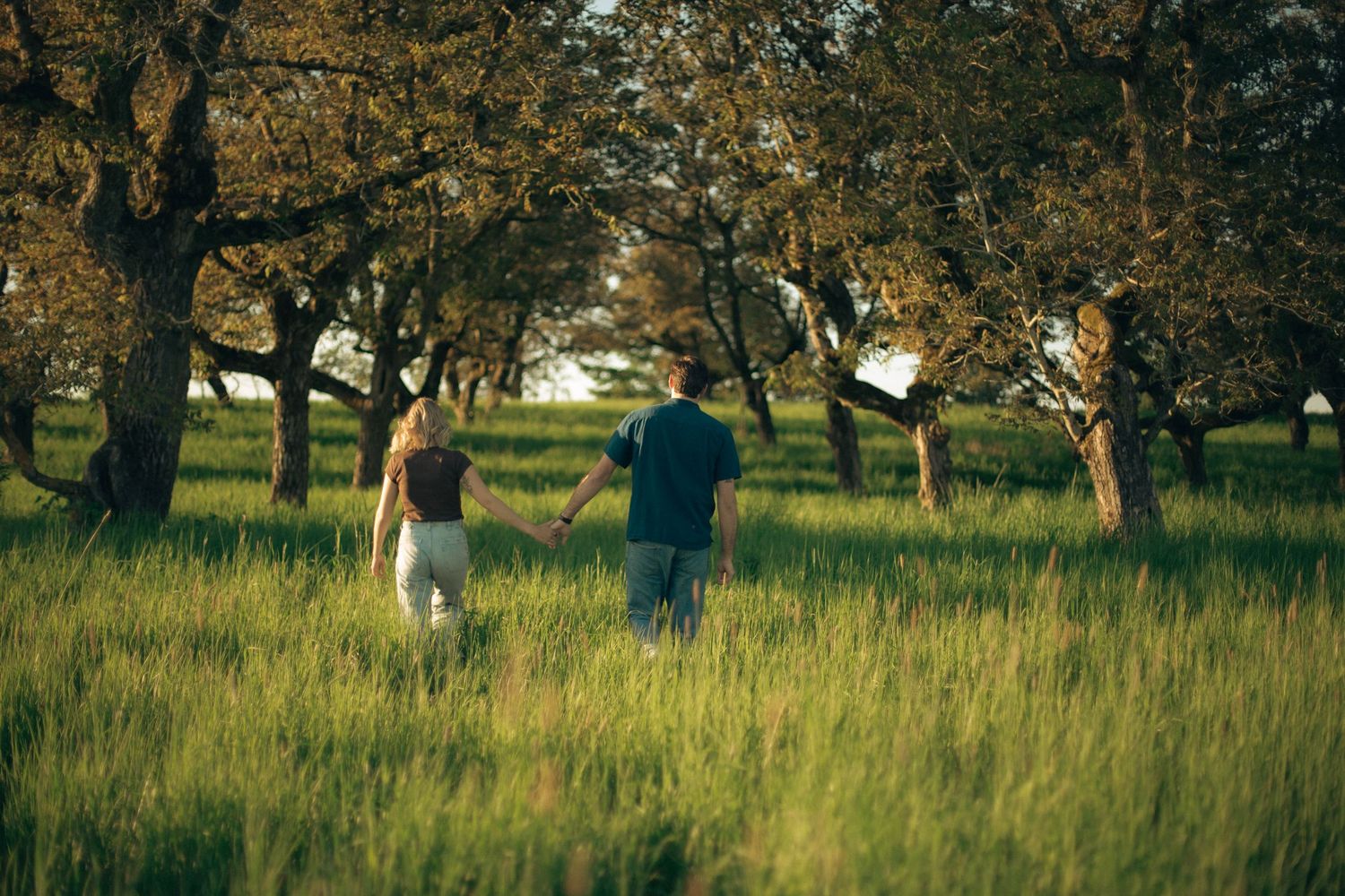 A couple walks holding hands through a field of tall grass