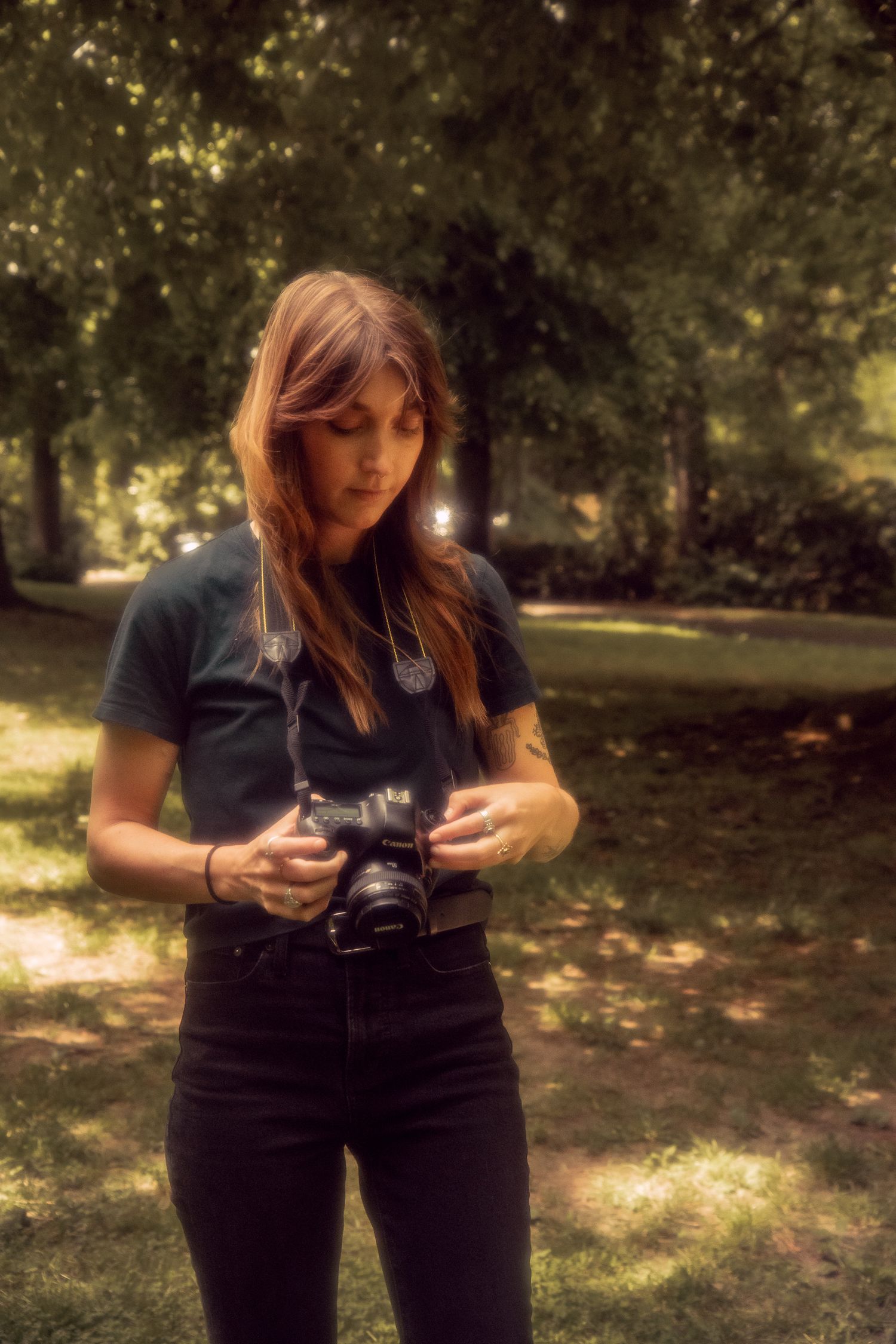 A photographer holds her camera at hip height and in front of trees in a park in Portland, Oregon