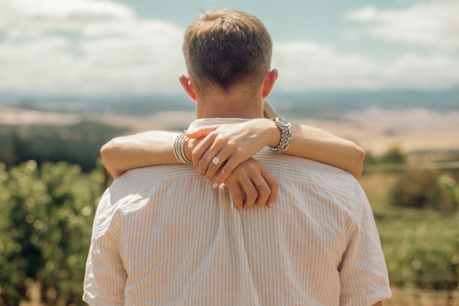 A woman wraps her hands around her fiancé's neck to show off her new engagement ring.