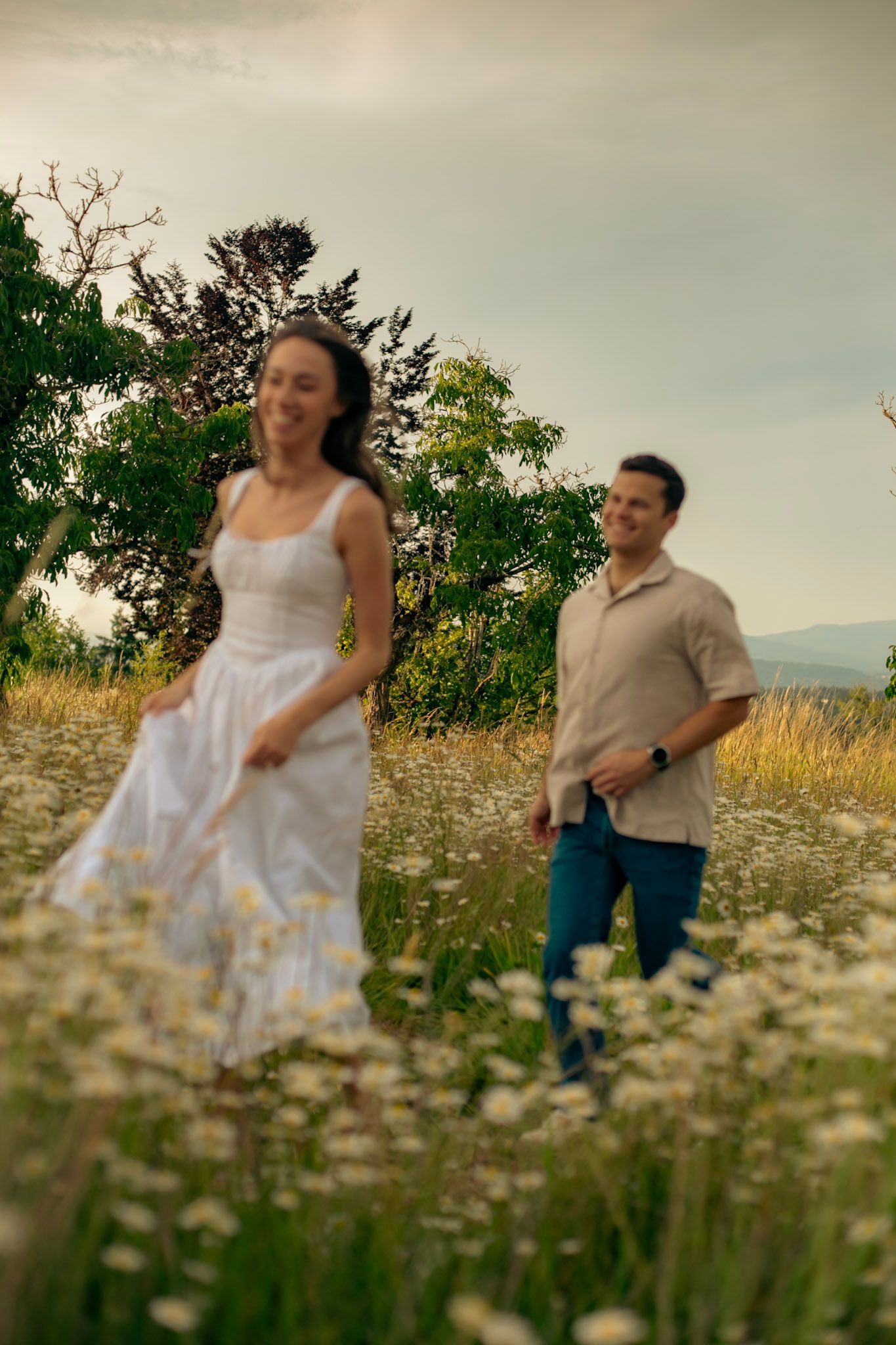 A man playfully chases his fiance in a field of wildflowers