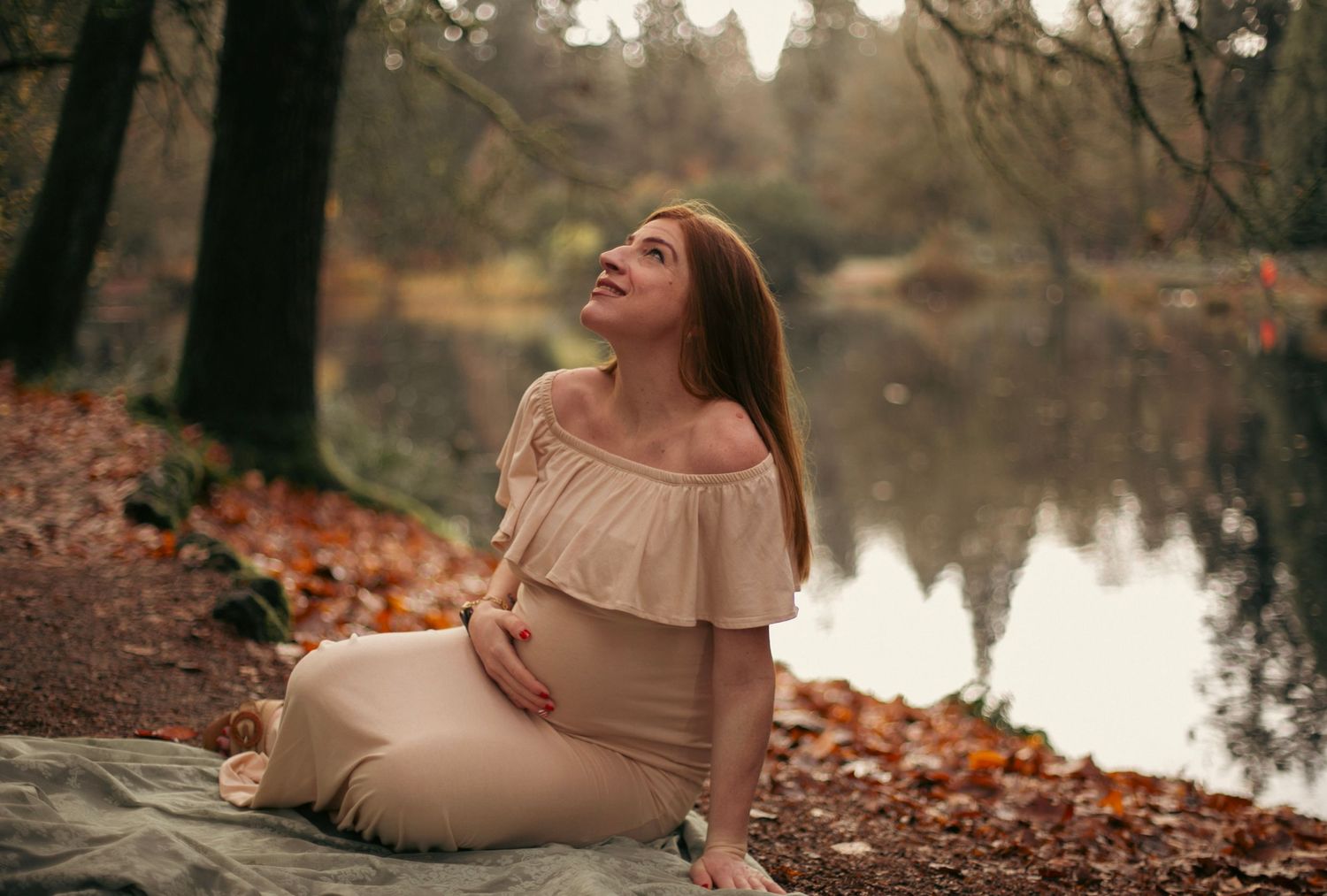 maternity photoshoot for a woman in a pink dress at a portland oregon park with water and leaves in the background