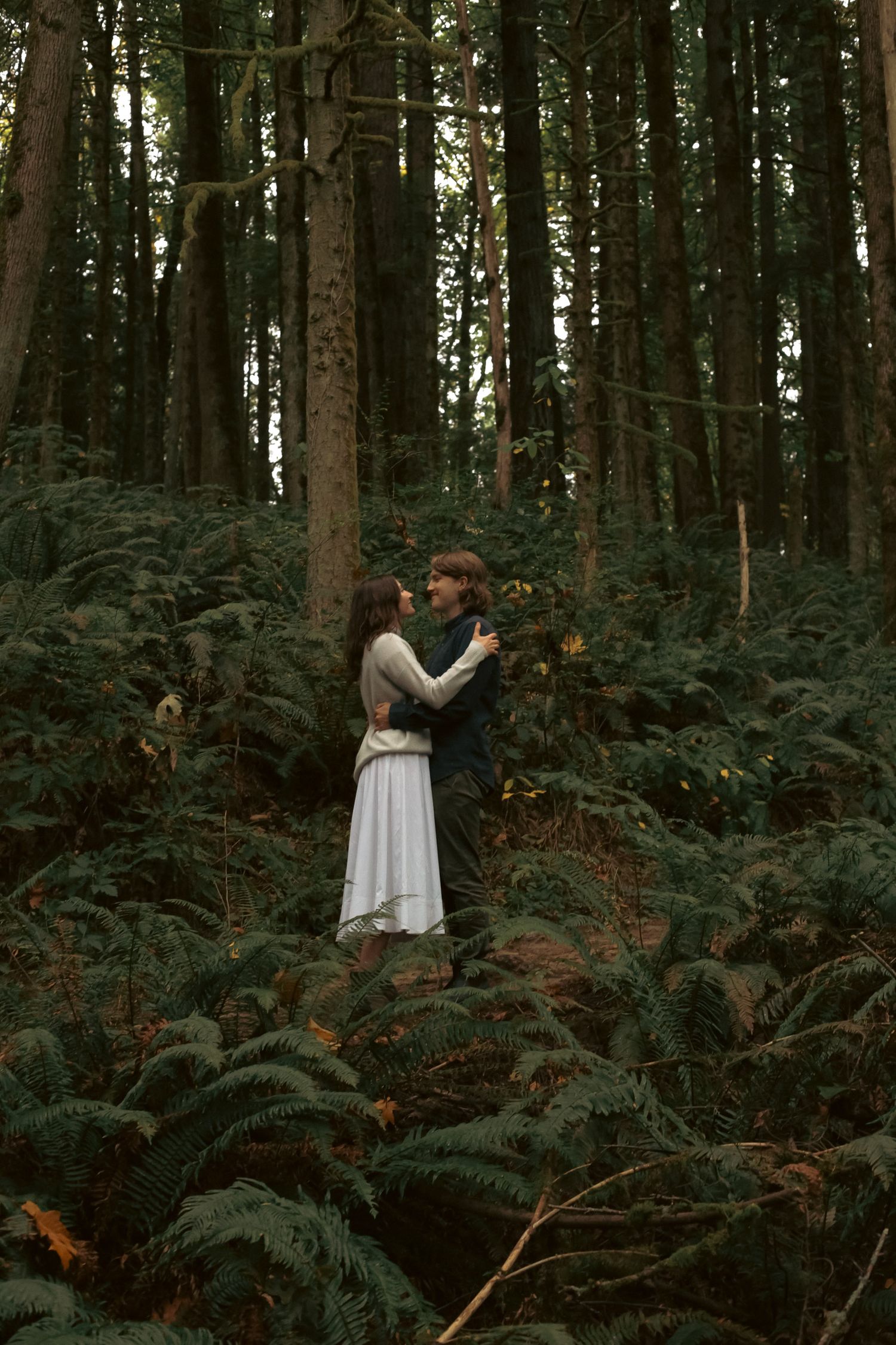 A young newly married couple embrace each other amongst a moody, green, lush forest backdrop for an elopement photoshoot