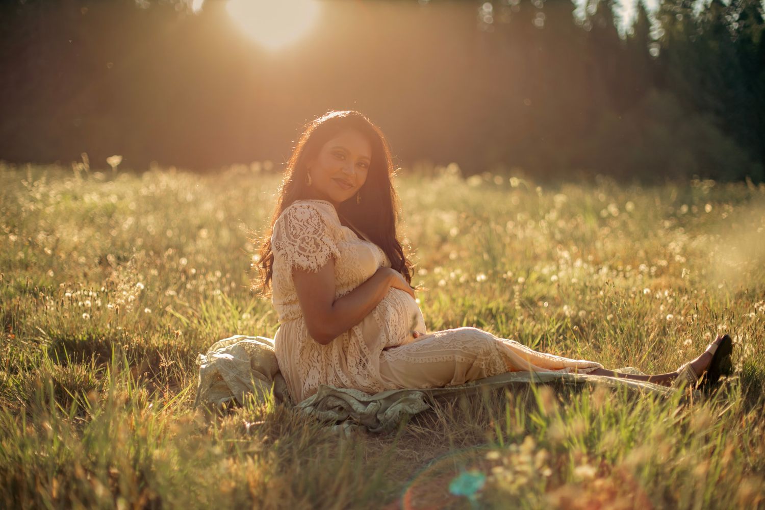 A woman hold her pregnant belly in a sunny field of flowers
