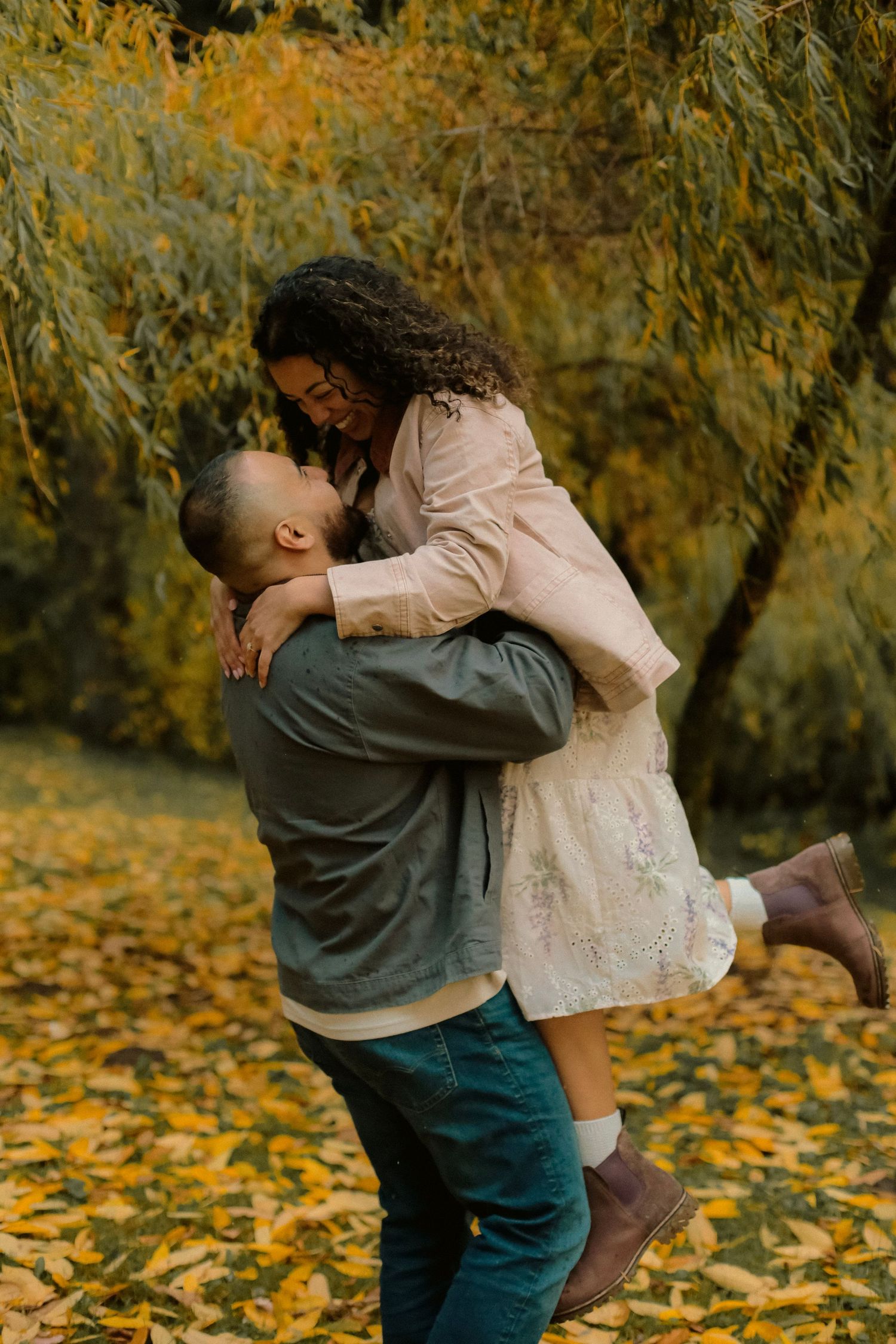 A man picks up his fiancé and swings her around with falling yellow leaves in the background.
